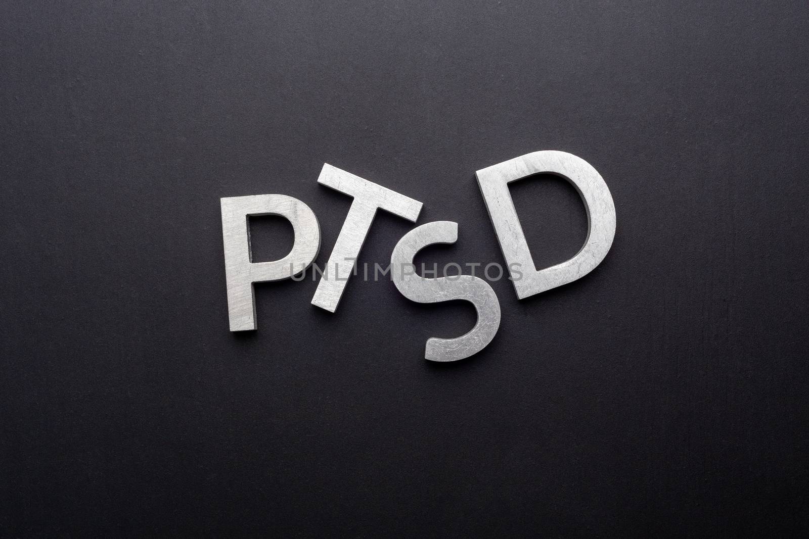 the word PTSD - post traumatic stress disorder - laid with silver metal letters on flat black background in directly above perspective