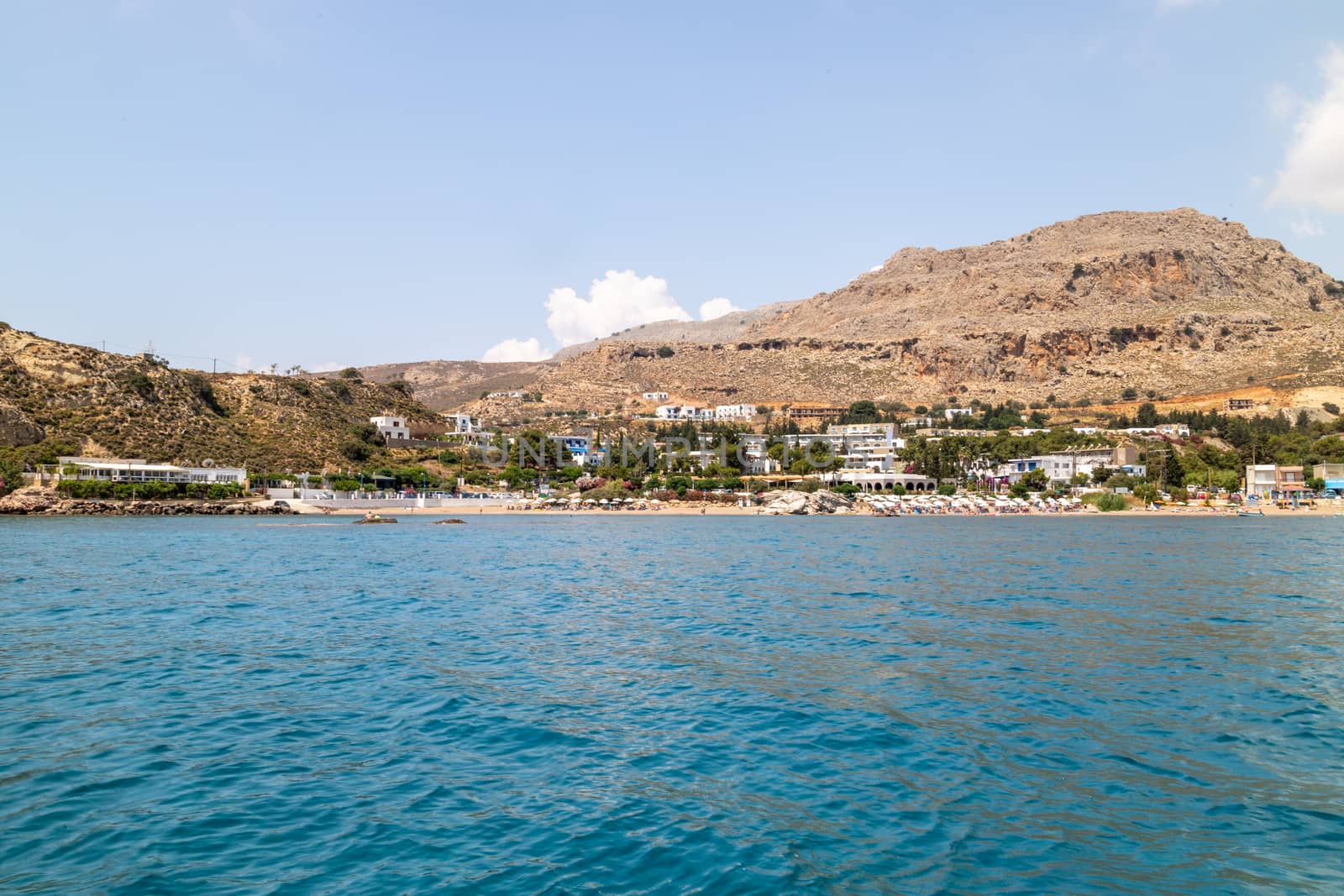 View from a boat on the water at Stegna beach with the mediterranean sea in the foreground and mountain range in the background on a sunny day in spring