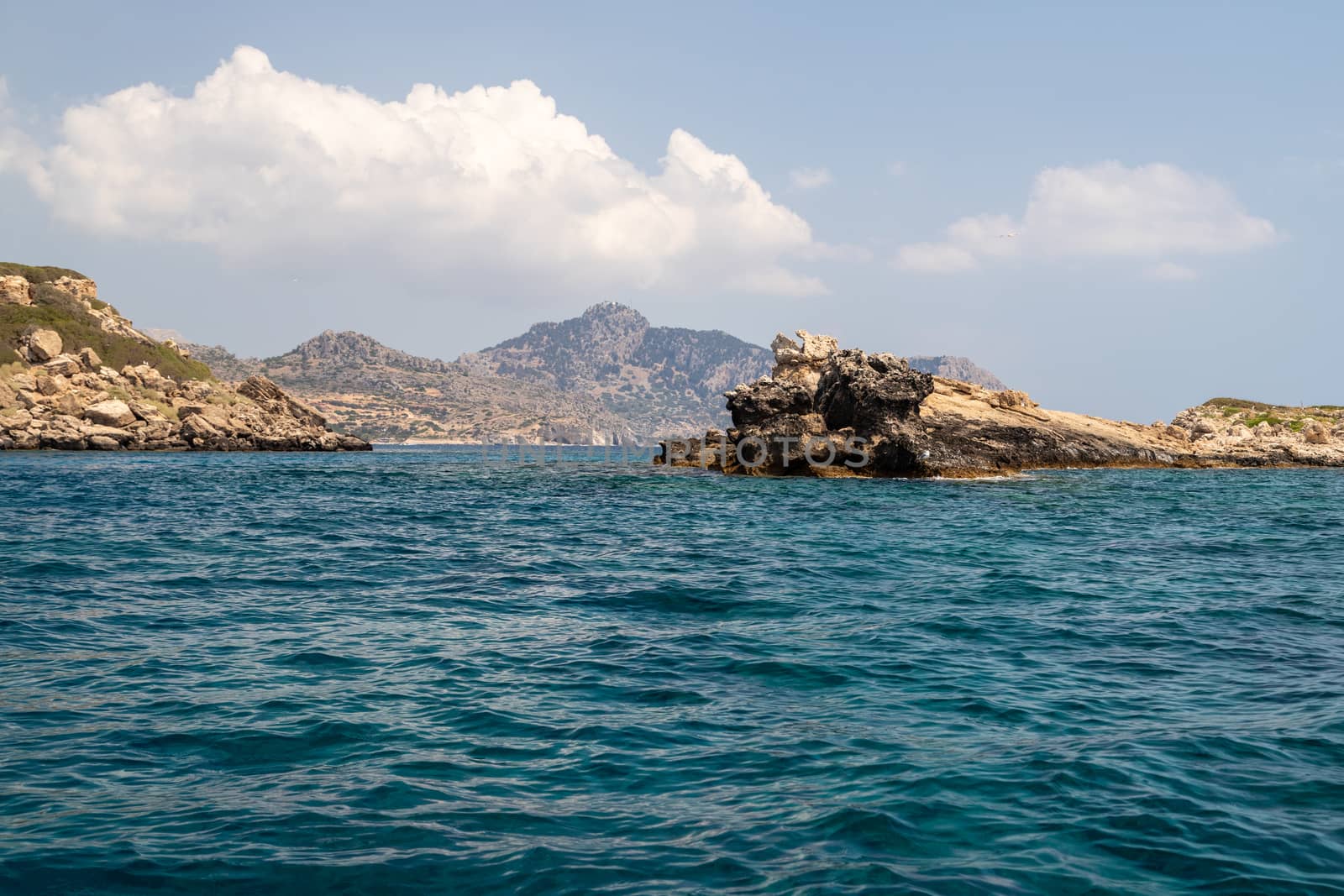 View from a motor boat on the mediterranean sea at the rocky coastline near Stegna on the eastside of Greek island Rhodes on a sunny day in spring