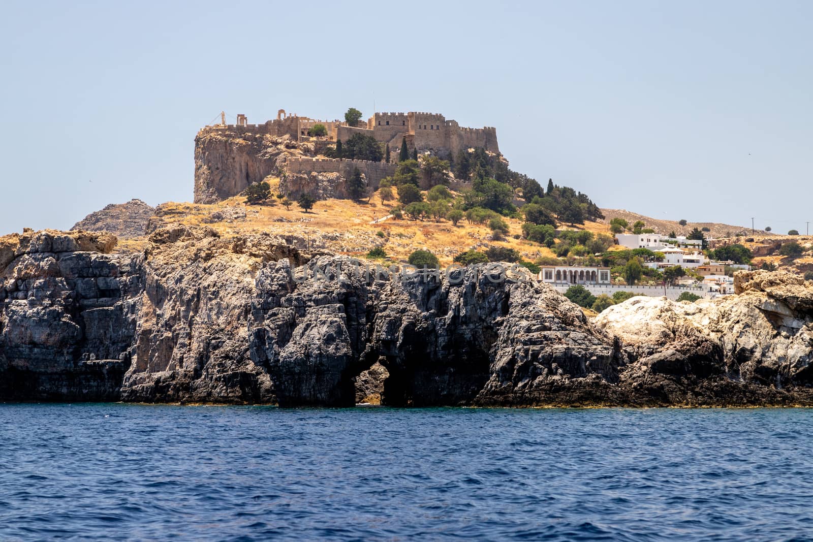 View from a motor boat on the mediterranean sea at the rocky coastline and the acropolis of Lindos near Stegna on the eastside of Greek island Rhodes on a sunny day in spring