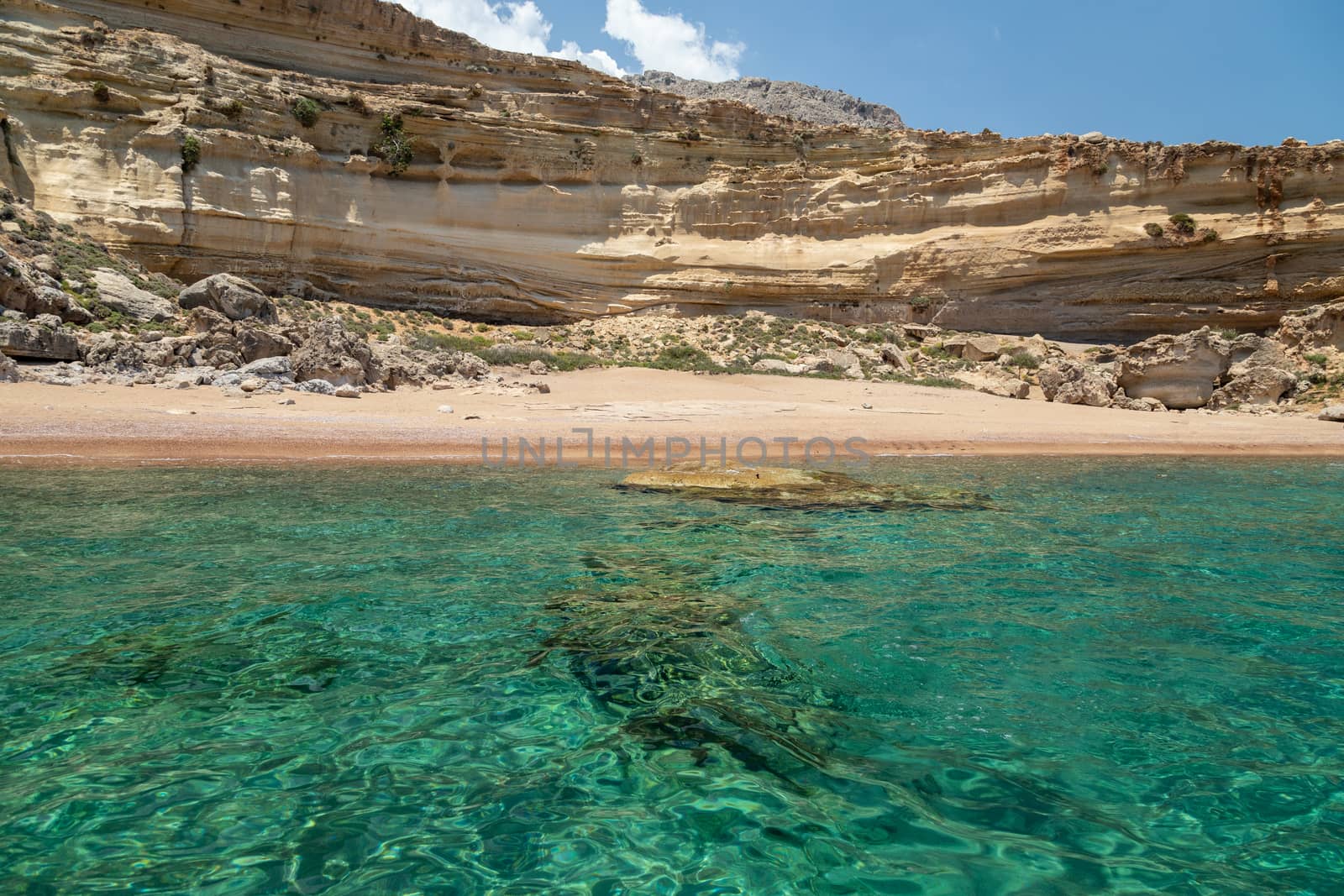 View from a motor boat on the mediterranean sea on the rocky coastline with red sand beach and clear turquoise water near Stegna on the eastside of Greek island Rhodes on a sunny day in spring