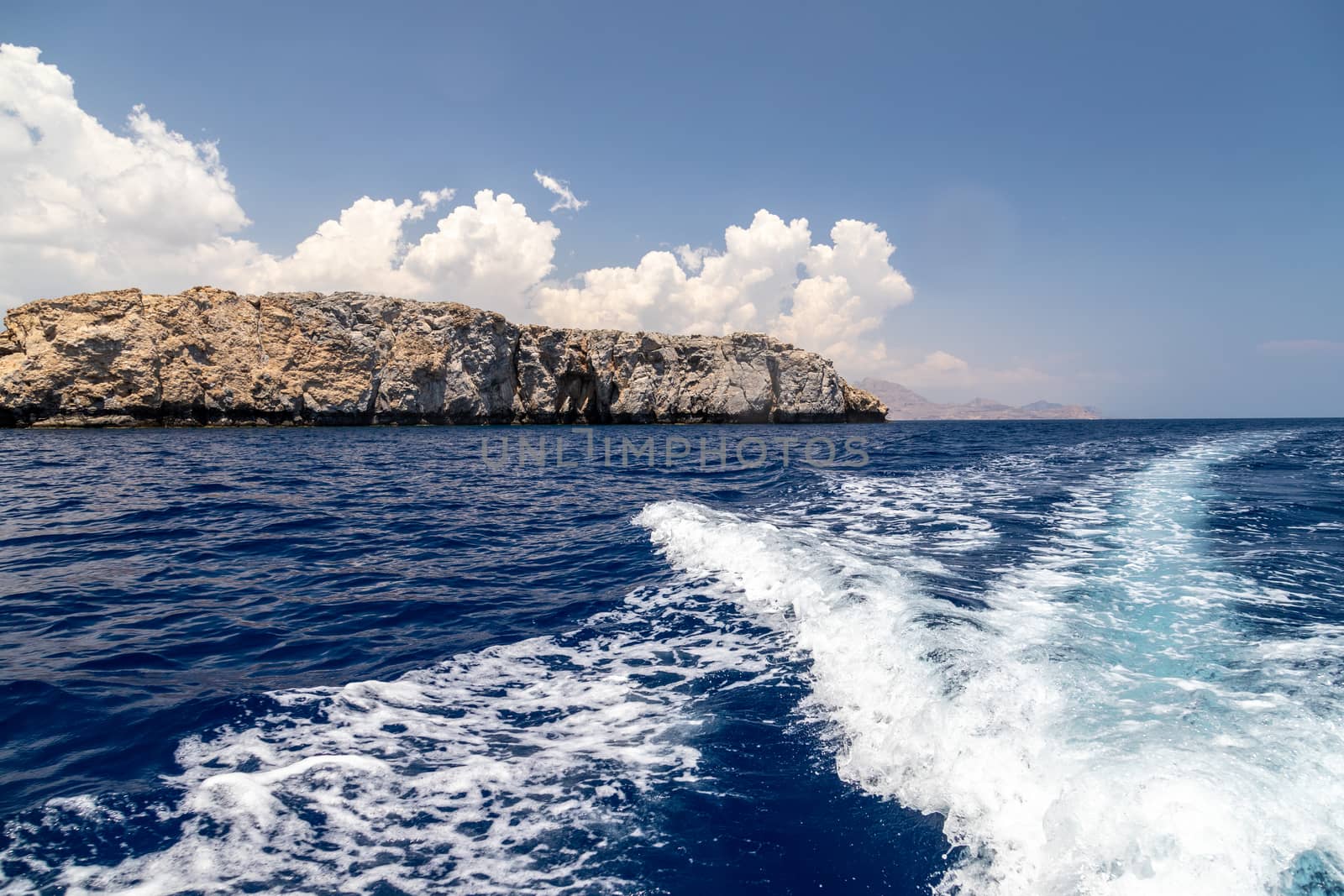 Stern wave of a motor boat with the motor in foreground and the rocky coastline on the eastside of Greek island Rhodes in the background on a sunny day in spring