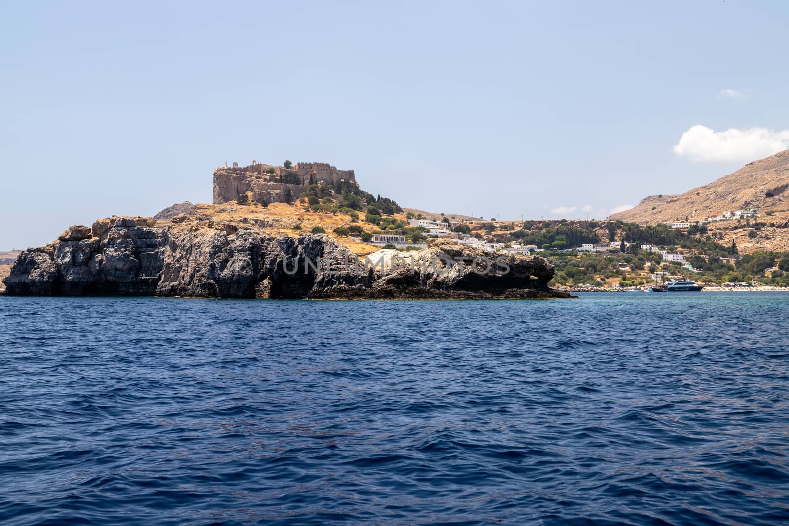 View from a motor boat on the mediterranean sea at the rocky coastline and the acropolis of Lindos near Stegna on the eastside of Greek island Rhodes on a sunny day in spring