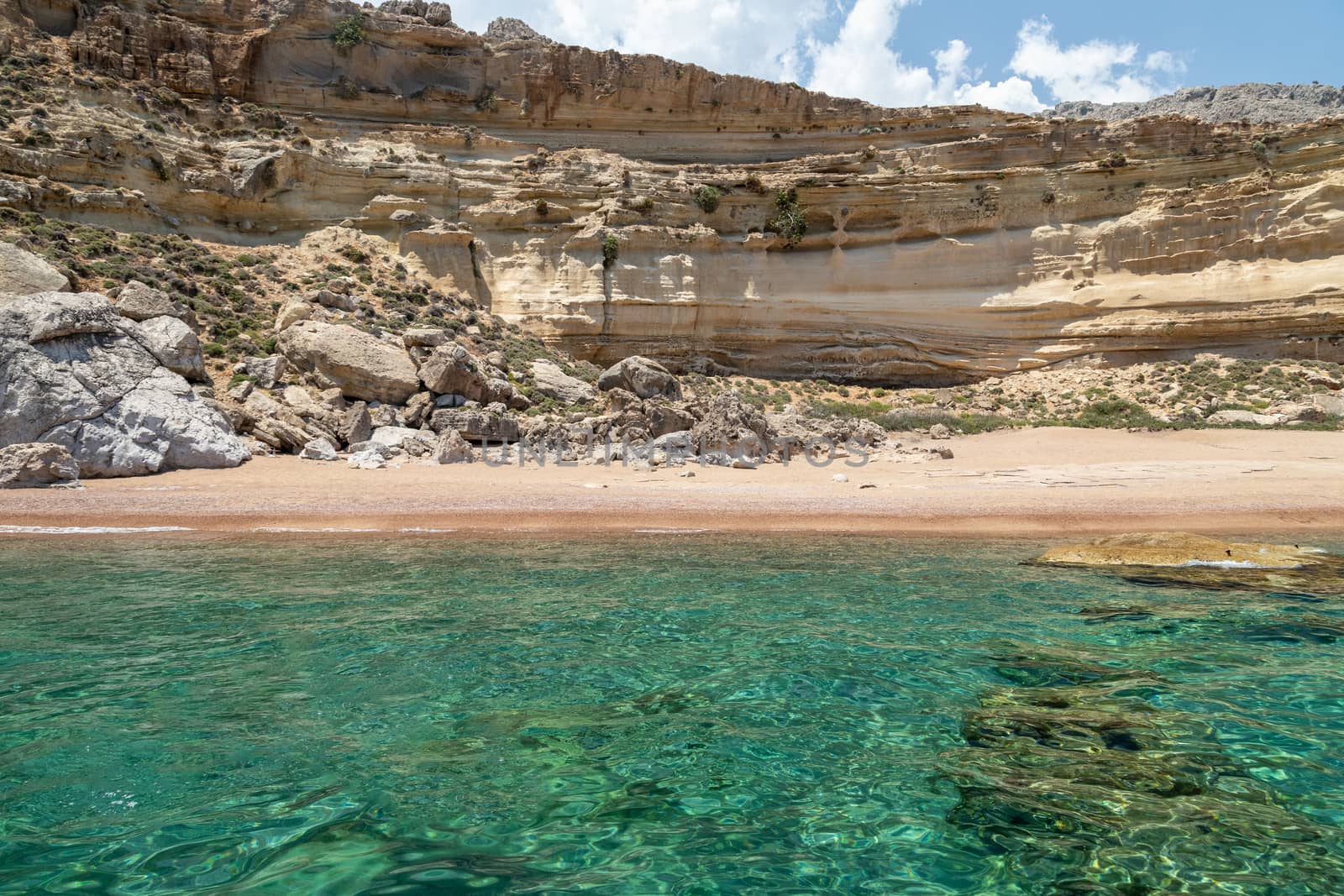 View from a motor boat on the mediterranean sea on the rocky coastline with red sand beach and clear turquoise water near Stegna on the eastside of Greek island Rhodes on a sunny day in spring