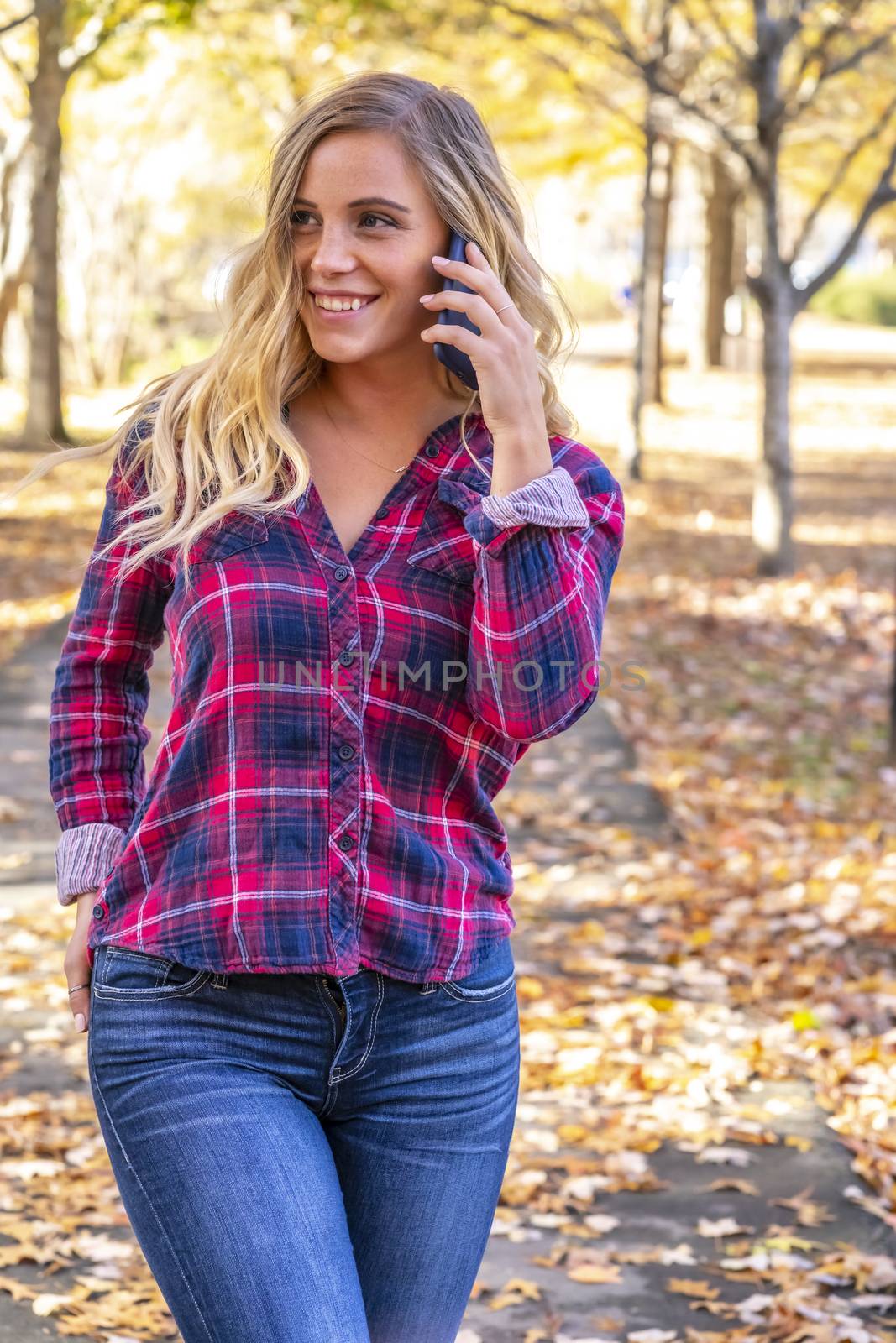 A Lovely Blonde Talks On Her Mobile Device On An Autumn Day Outdoors At The Park by actionsports