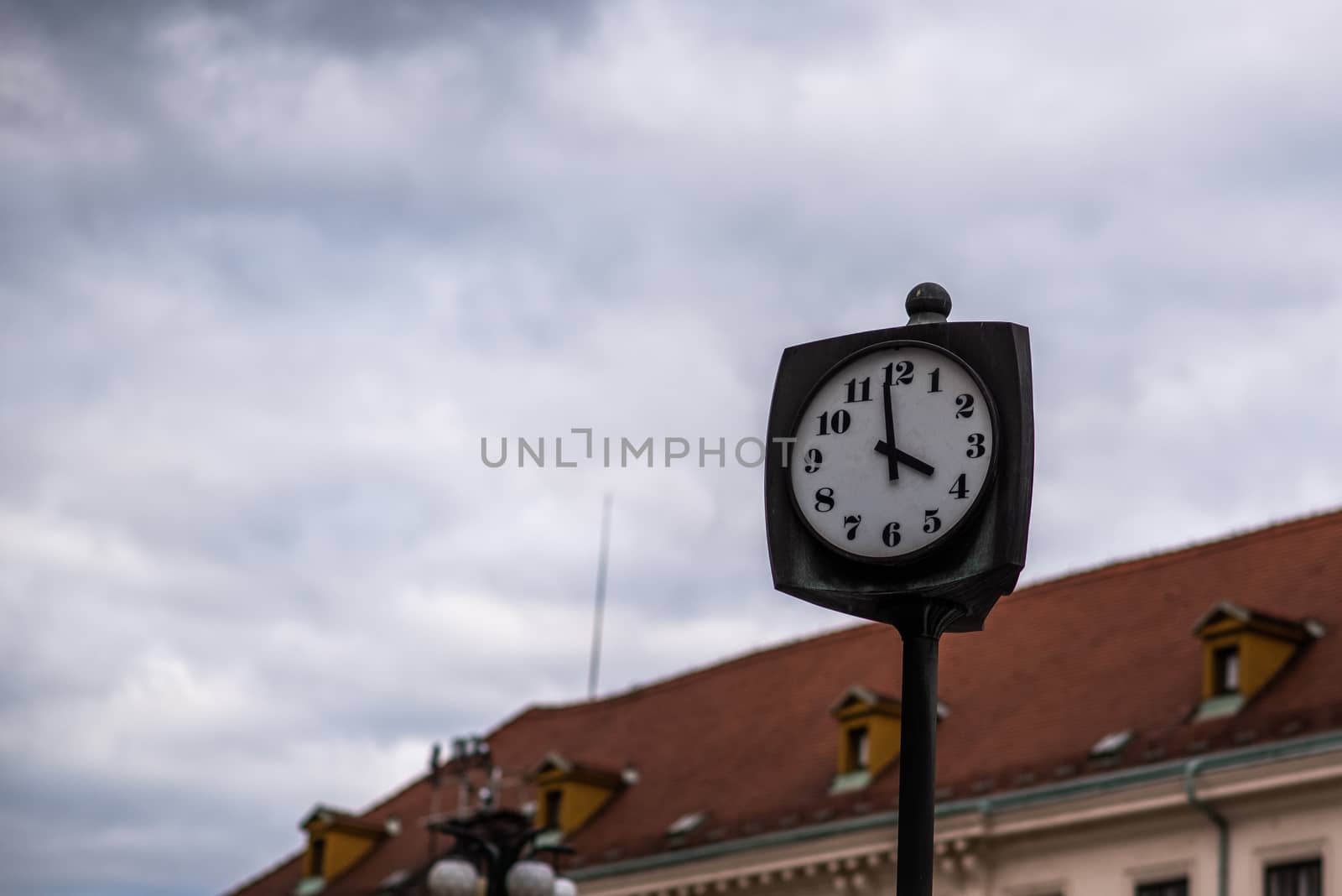 A clock outdoor in the city on a grey day with a building behind by gonzalobell