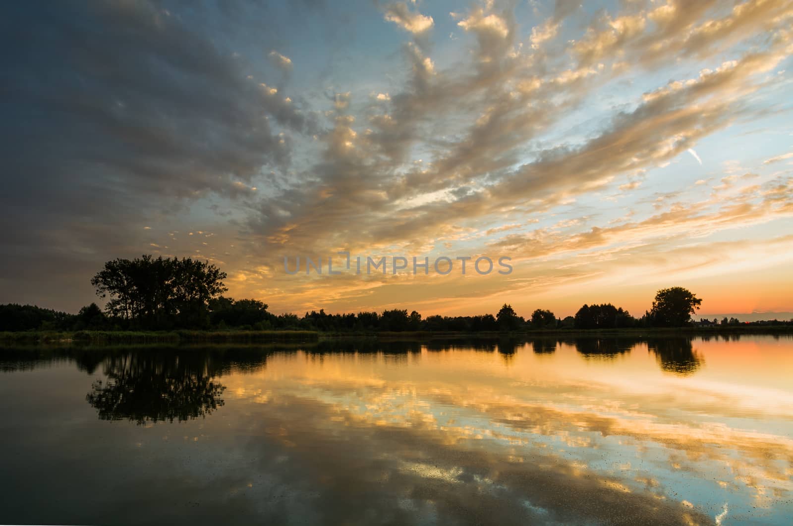 Reflection of clouds in water after sunset, shore and trees, evening view