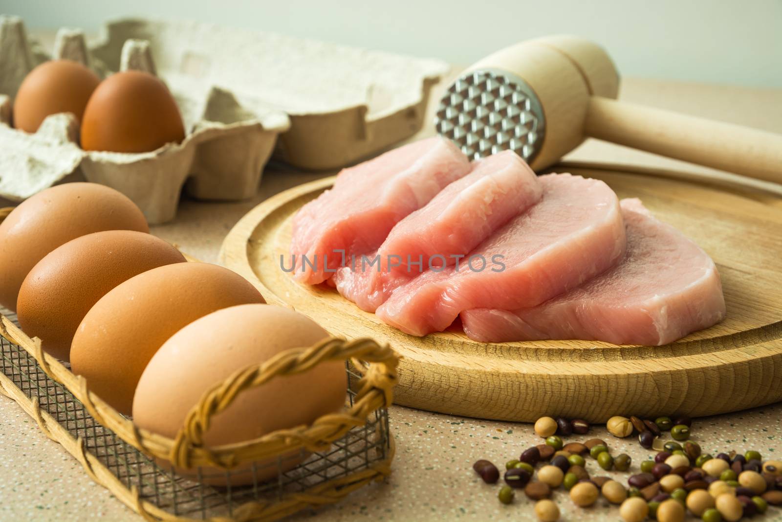 Raw loin meat on a wooden board, meat mallet and eggs