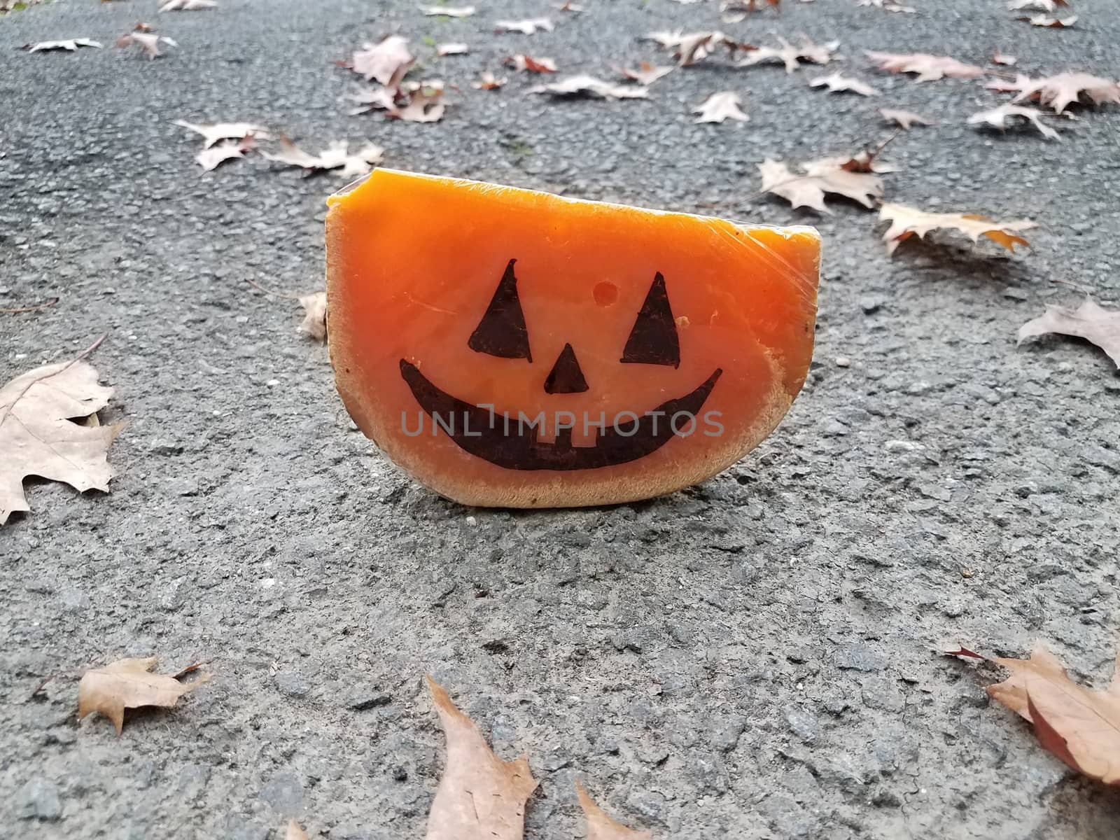 orange cheese with pumpkin face on asphalt with leaves