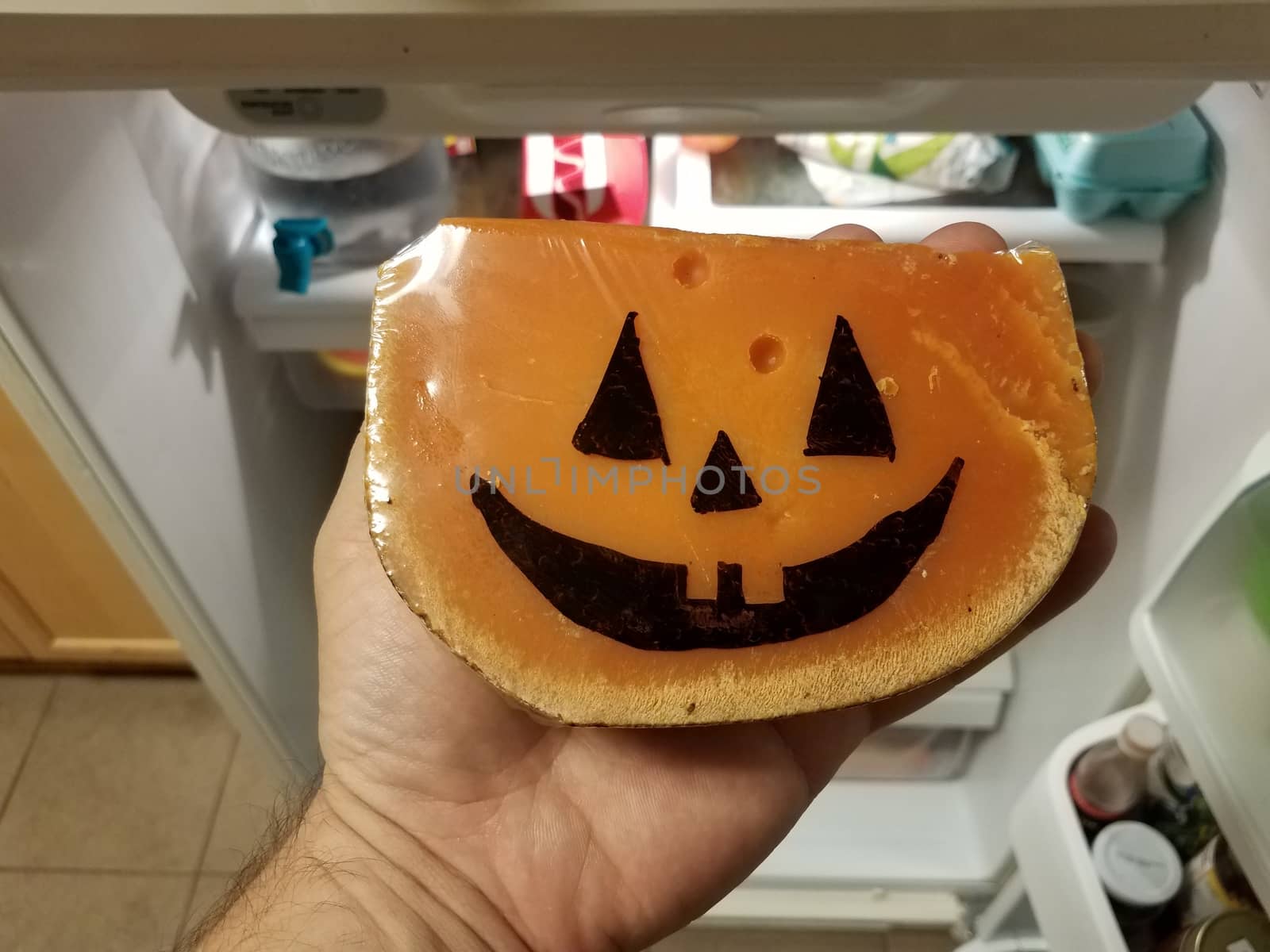 hand holding orange cheese with pumpkin face in refrigerator