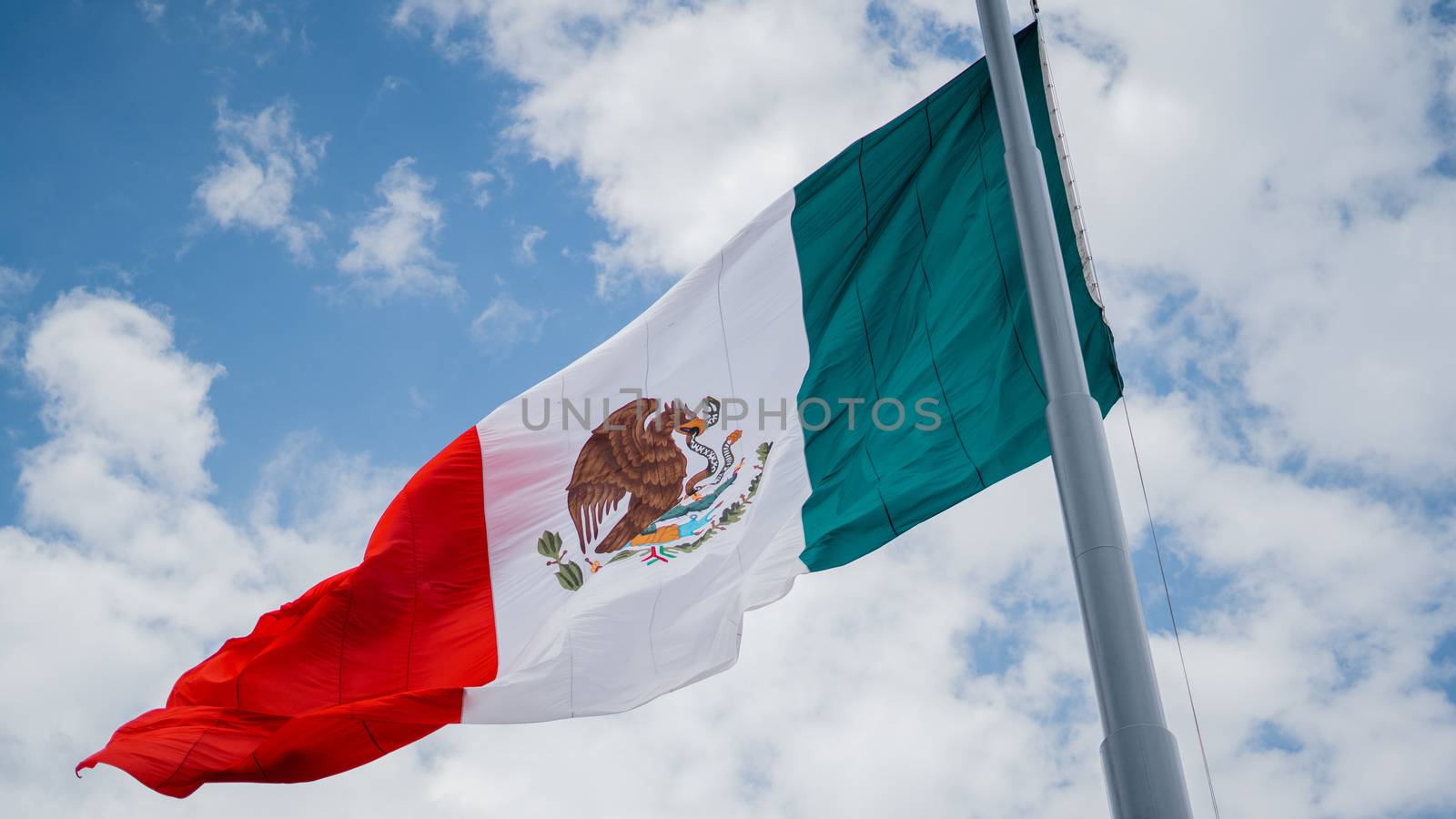 Picture of the Mexican Flag Waving in the Wind and a Slightly Cloudy Blue Sky as the Background