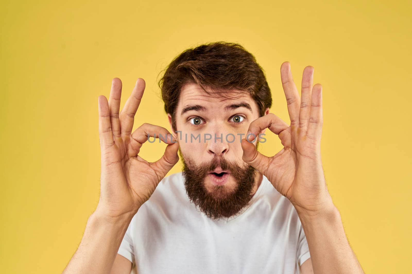 Bearded man emotions fun gesture with hands white t-shirt close-up yellow background by SHOTPRIME