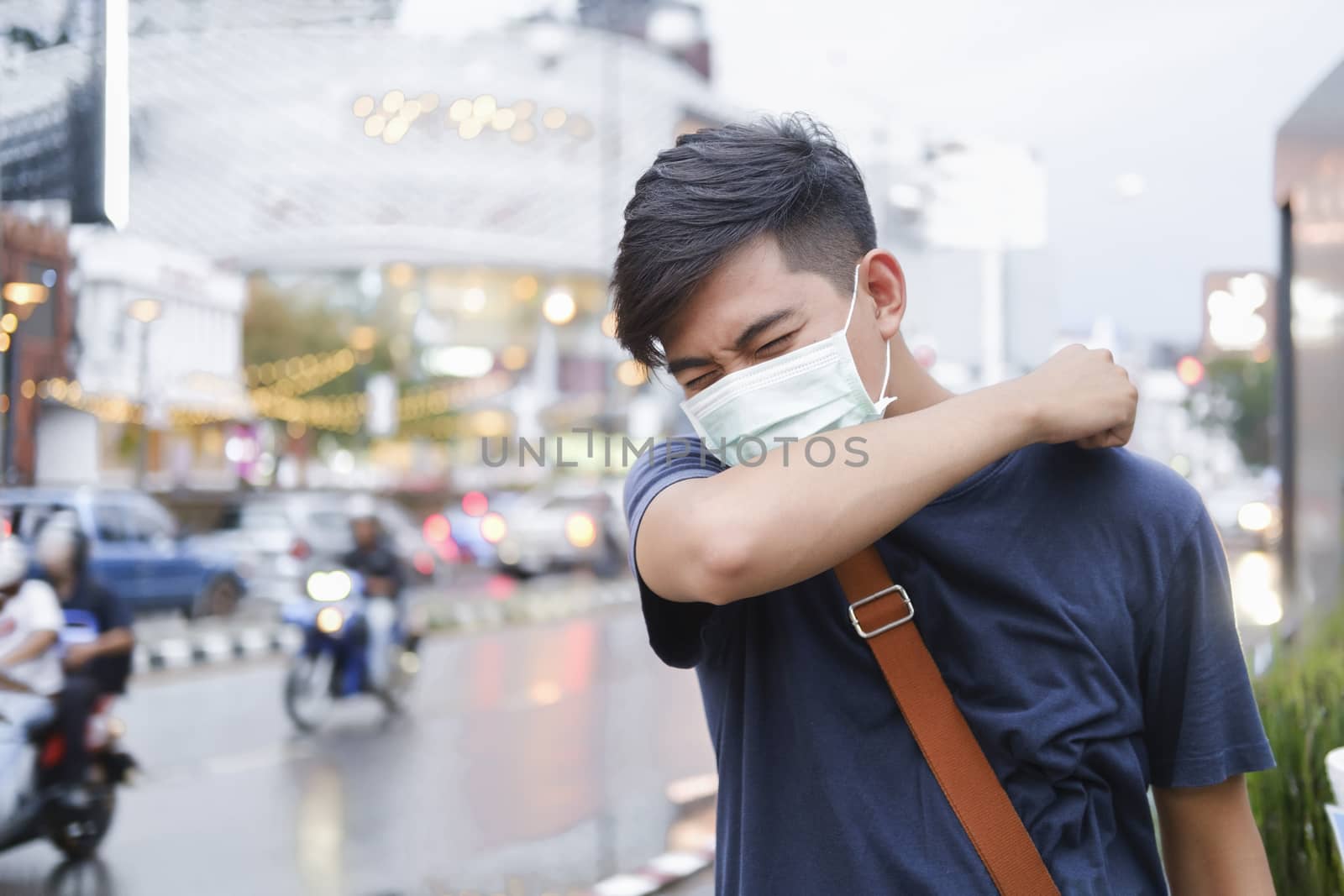 Close-up young man with protective face mask coughs in his elbow. Correct sneezing. Concept of stop spread of the virus.