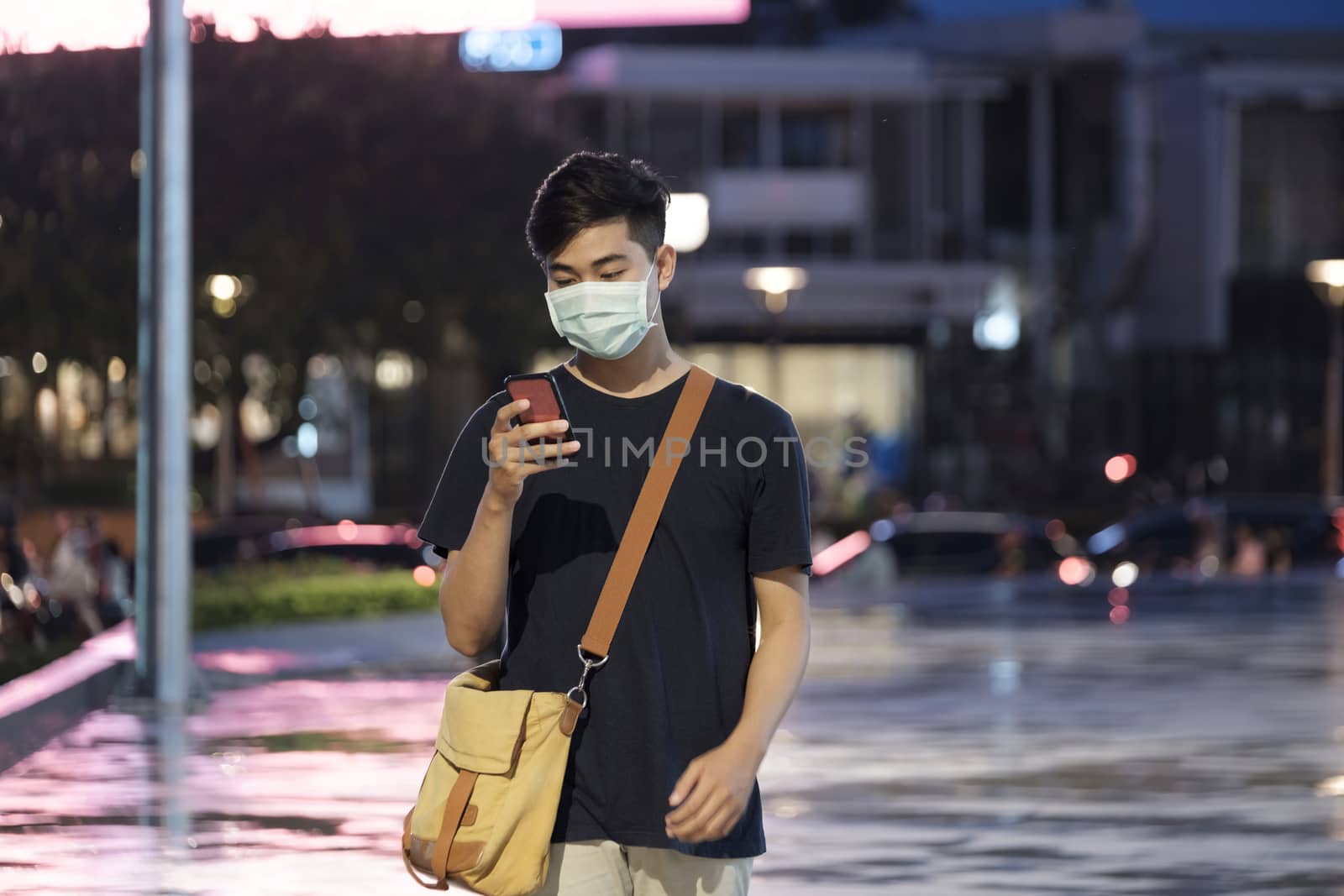 Young man with protective face mask using mobile phone in downtown city street prevent from the spread of viruses in the city. New normal concept.