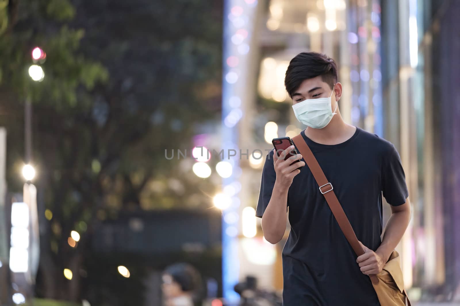 Young man with protective face mask using mobile phone in downtown city street prevent from the spread of viruses in the city. New normal concept.