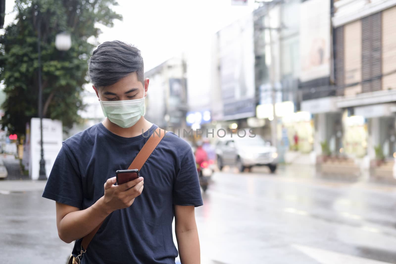 Young man with protective face mask using mobile phone in downtown city street prevent from the spread of viruses in the city. New normal concept.