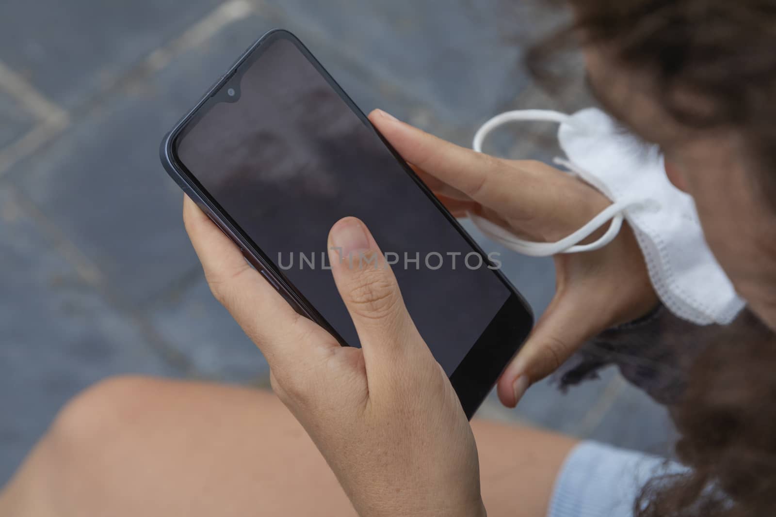 A young woman, grasping a face mask and a smart mobile phone, Spain. by alvarobueno