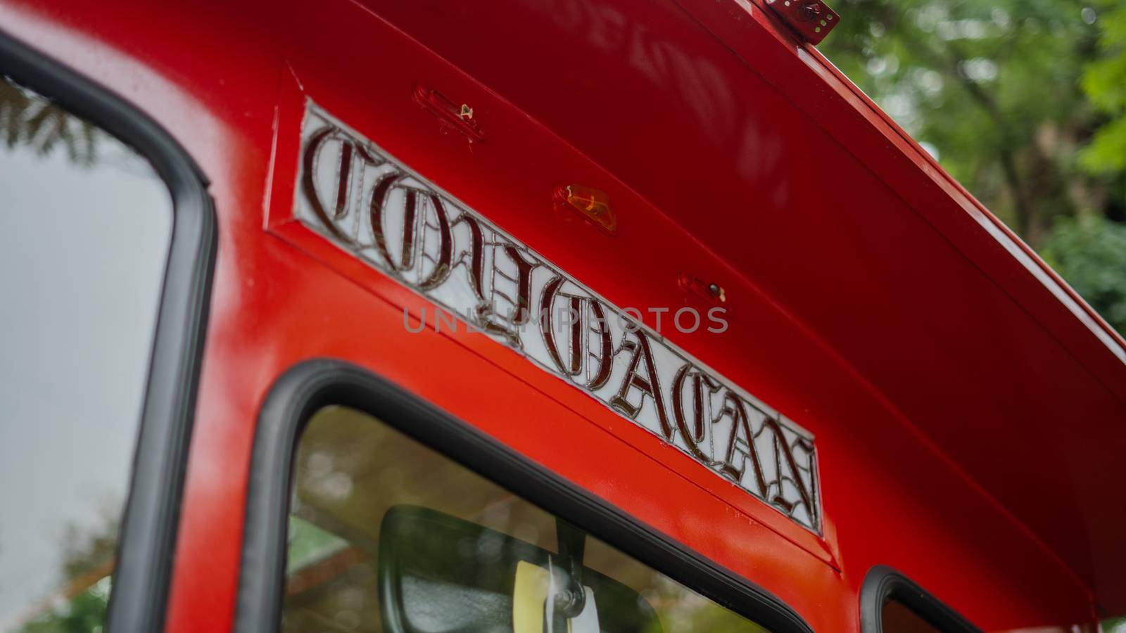 Picture of a Coyoacan Sign on a red and yellow trolley car driving on a street, with a blurry tree in the background