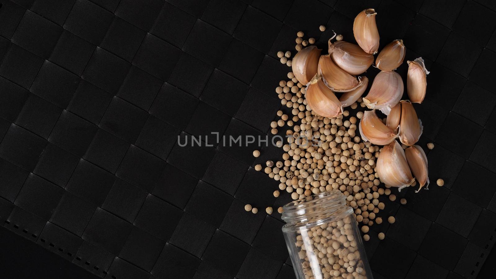 Natural Garlic and white peppercorn in glass bottle on plate mat black background in studio shot. It is main ingrediant for many asian recipe menu such as Singapore Bak kut teh, Thailand’s Pad Thai and more.