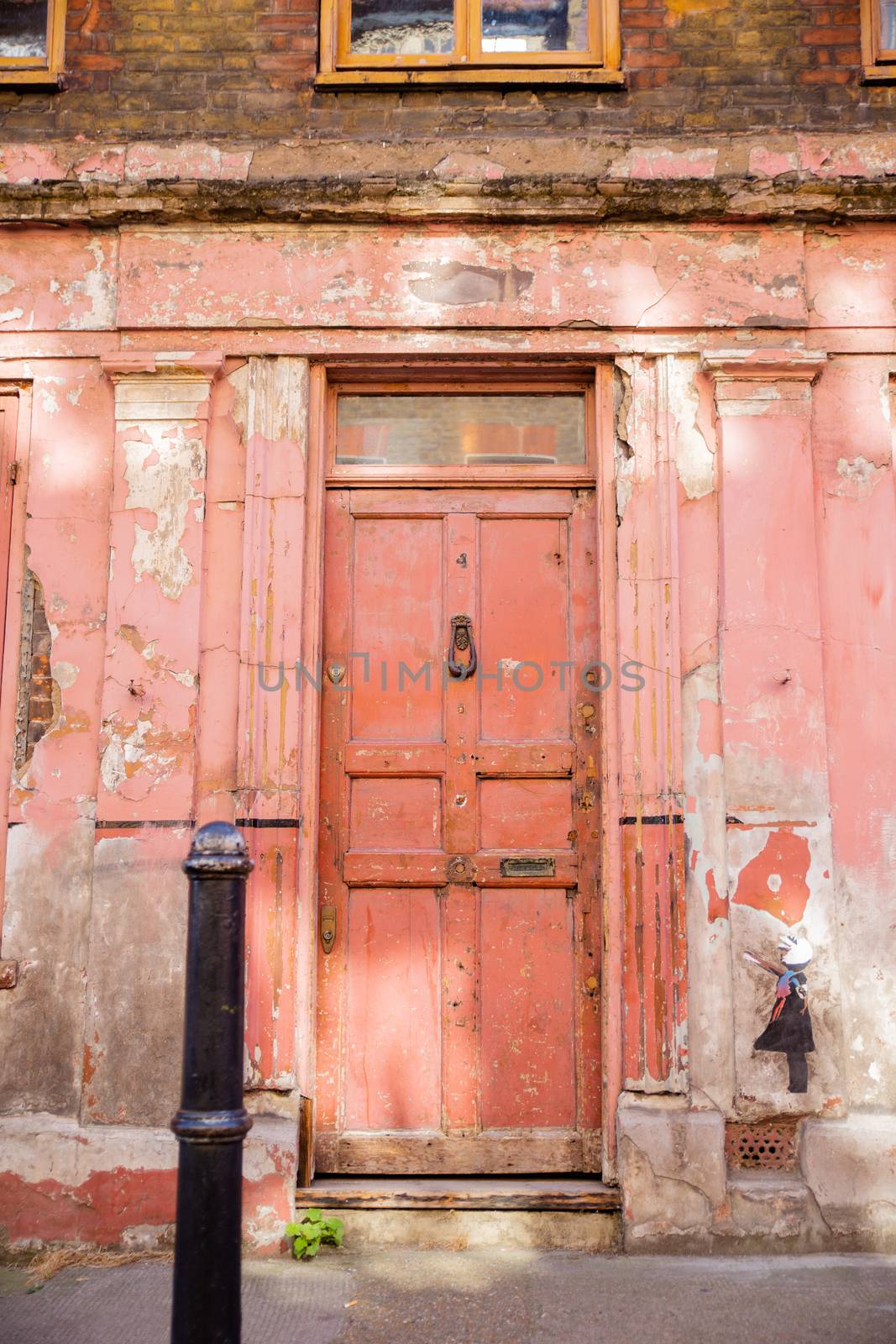 Portrait View of a Deteriorated Red Door on a building with a little girl painted on a wall