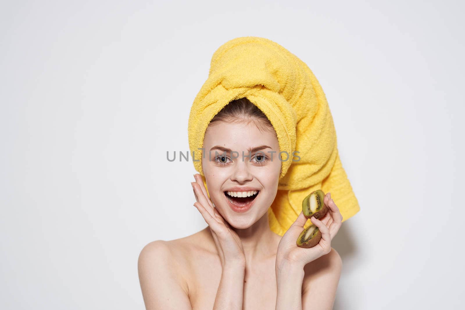 Cheerful woman with a yellow towel on her head bare shoulders of kiwi in her hands. High quality photo