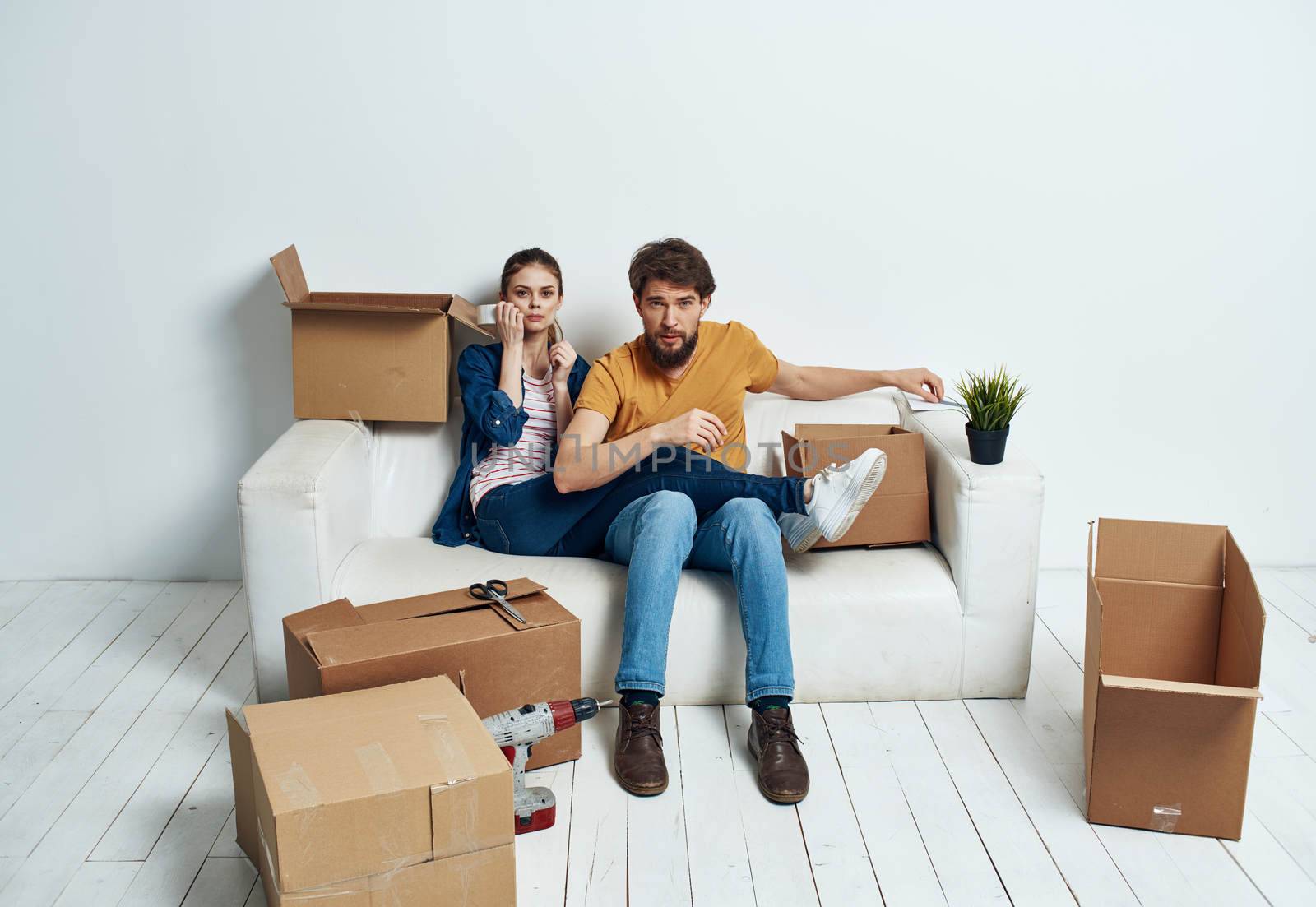 Married couple on a white sofa in the room interior with boxes of communication things. High quality photo