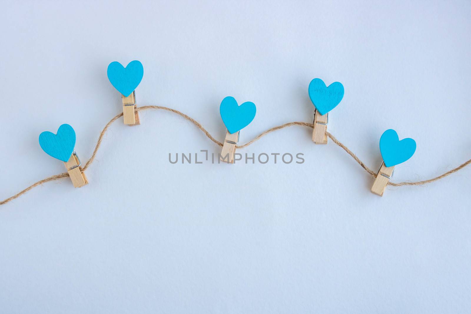 Small clothespins and blue hearts on a string on a white background.