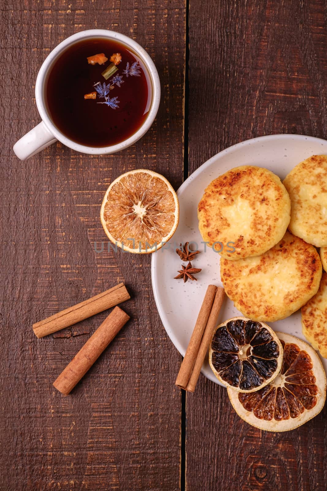 Cottage cheese fritters with hot black aromatic tea, Christmas breakfast mood with anise, cinnamon and dried citrus on wooden background, top view