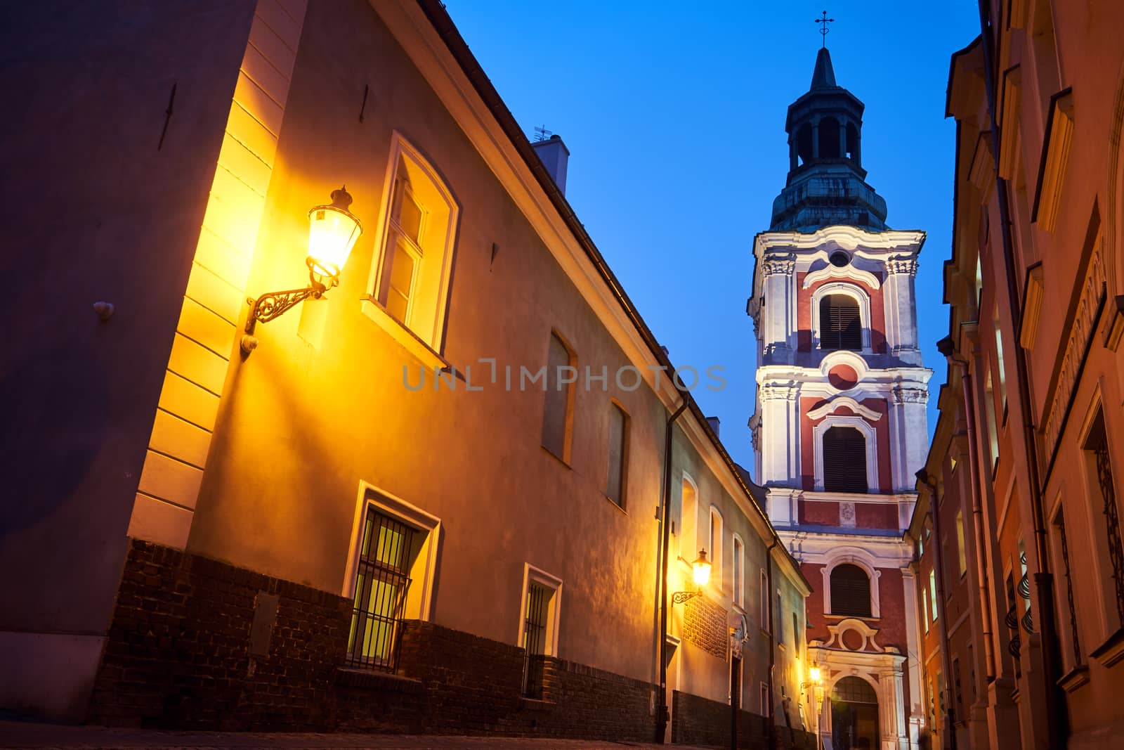 narrow street and belfry of the baroque historic church at night in Poznan