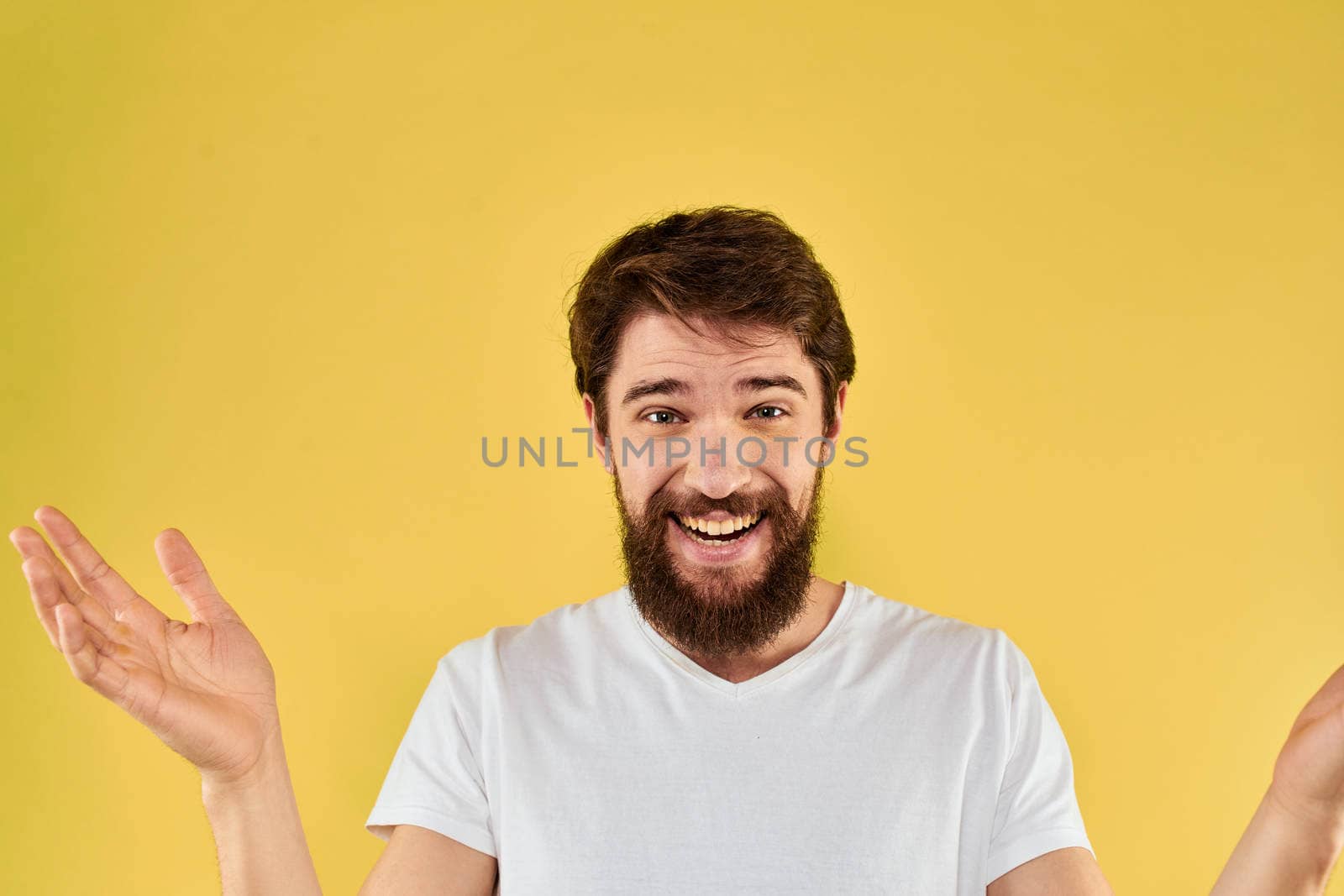 Bearded man emotions fun gesture with hands white t-shirt close-up yellow background. High quality photo