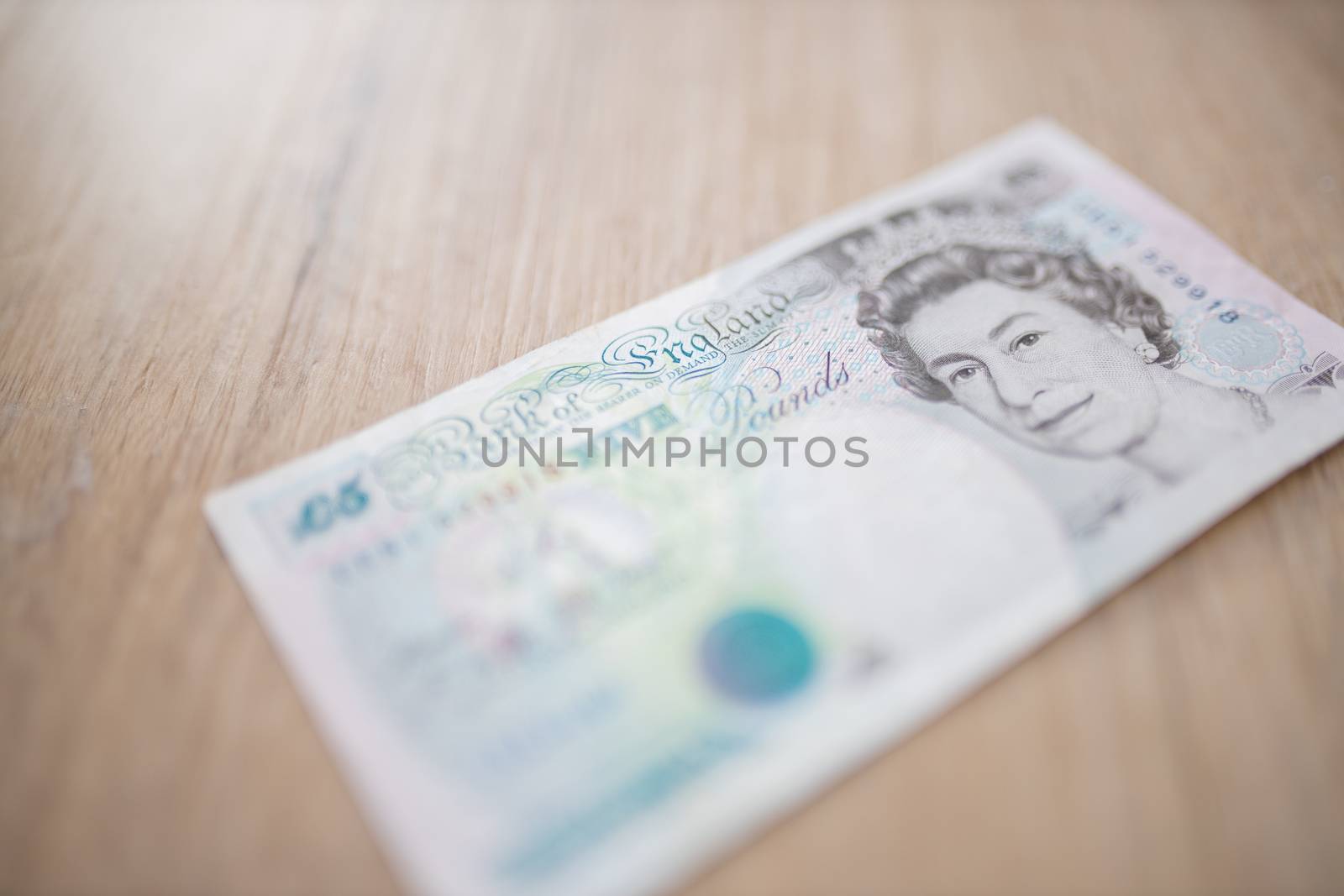 Picture of a Five Pounds Banknote with the face of Queen Elizabeth II, on a Wooden Table