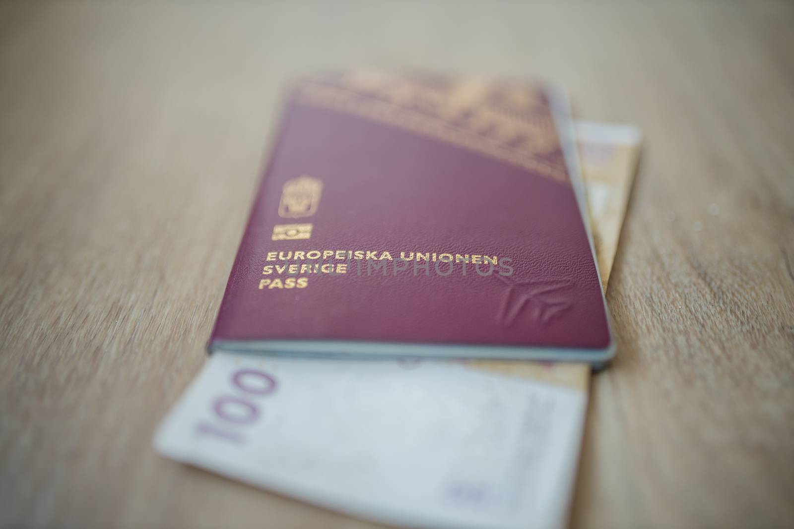 Picture of a Swidish Passport -with the words European Union Sweden Passport in Swedish- with a 100 Moroccan Dirhams Bill Partially Inside