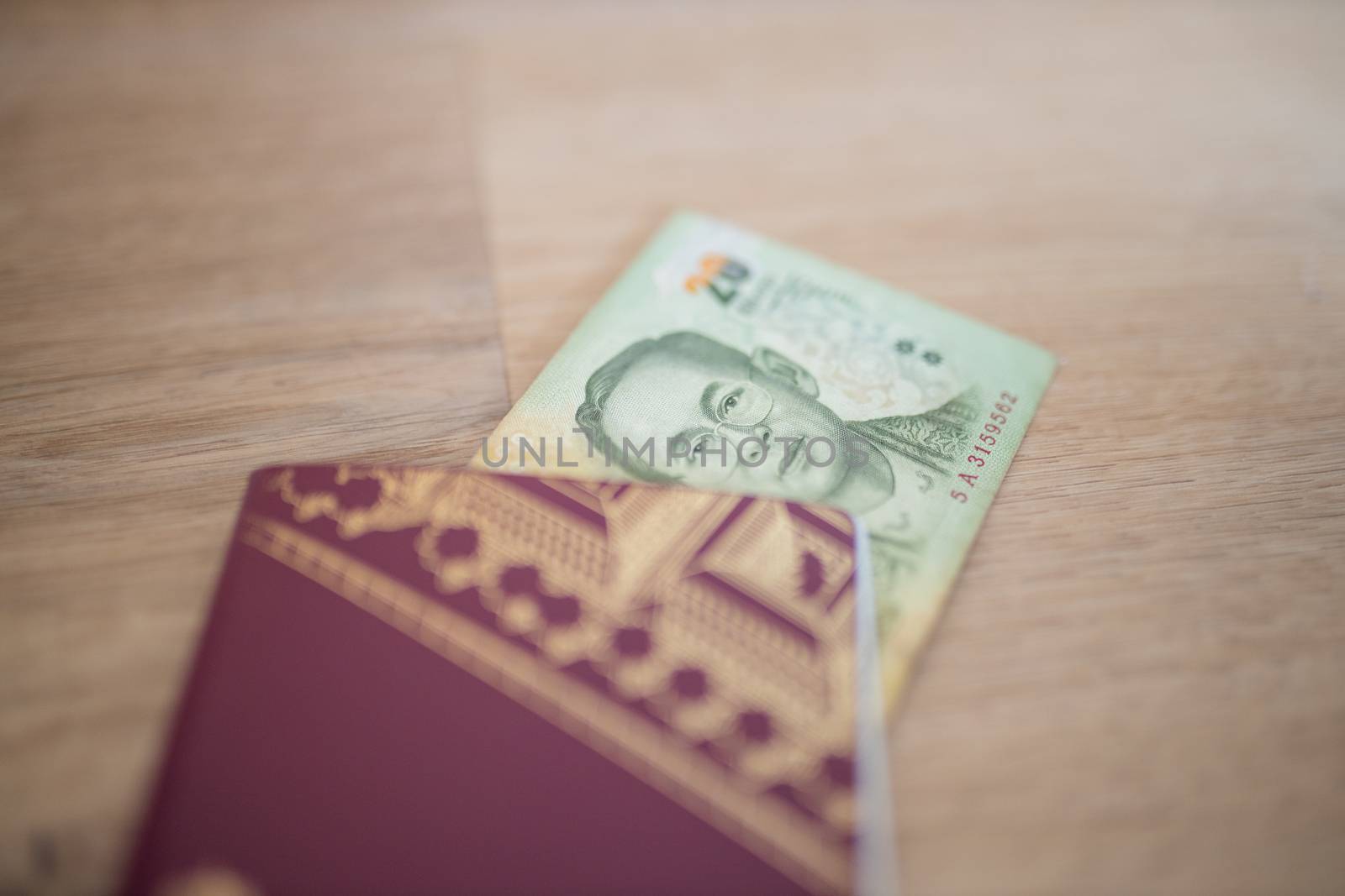 Picture of a 20 Thai Baht Bill Partially Inside a blurry Sweden Passport, showing the face of Bhumibol Adulyadej