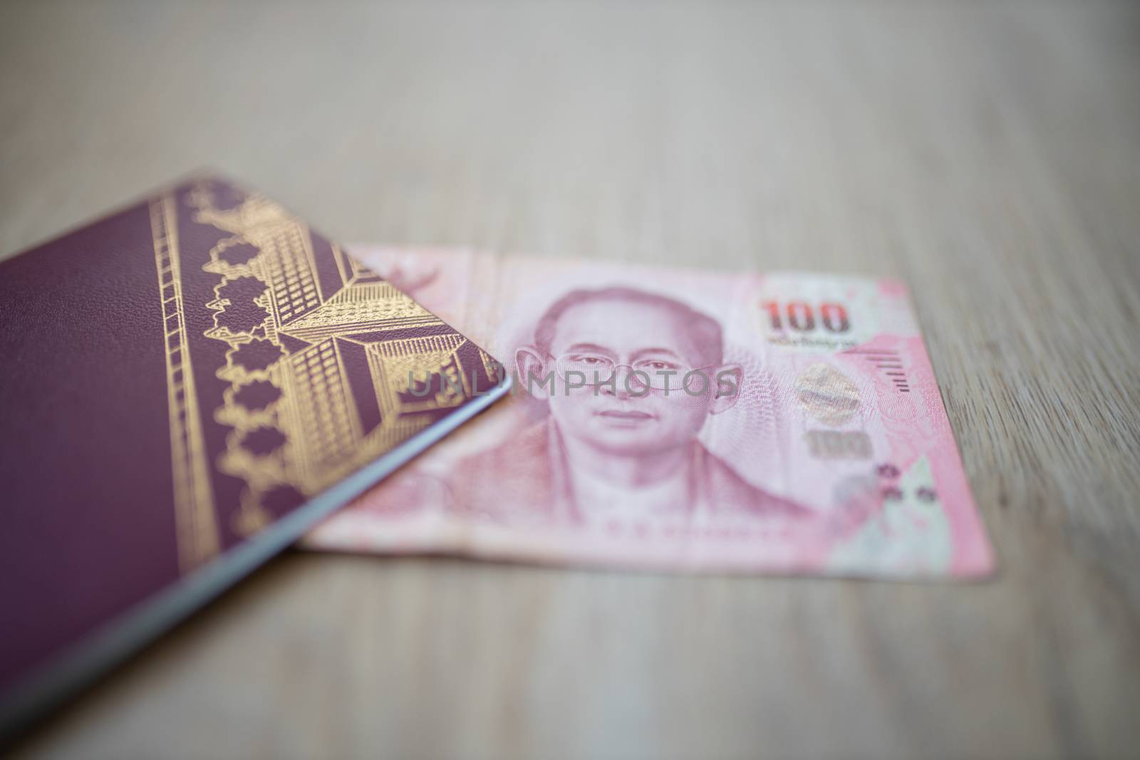 Picture of a 100 Thai Baht Bill Partially Inside a blurry Sweden Passport, showing the face of Bhumibol Adulyadej
