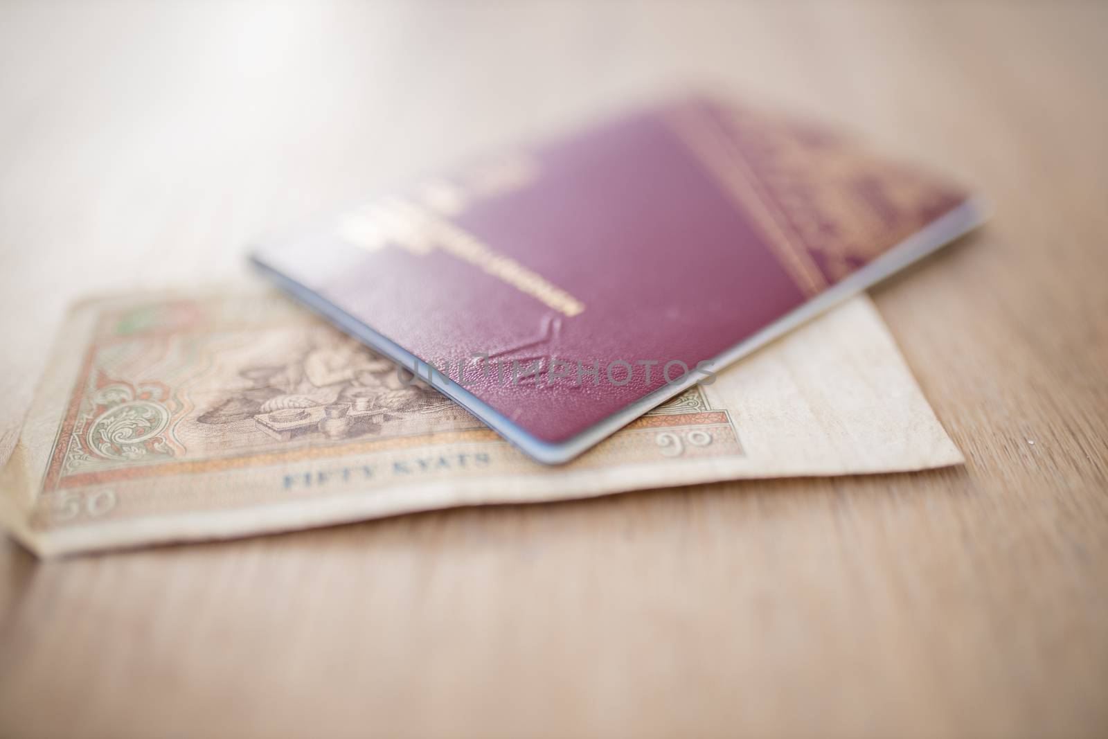 Picture of a Fifty Burmese Kyats Bill with the number 50 in Burmese and partially Inside a Blurry Sweden Passport