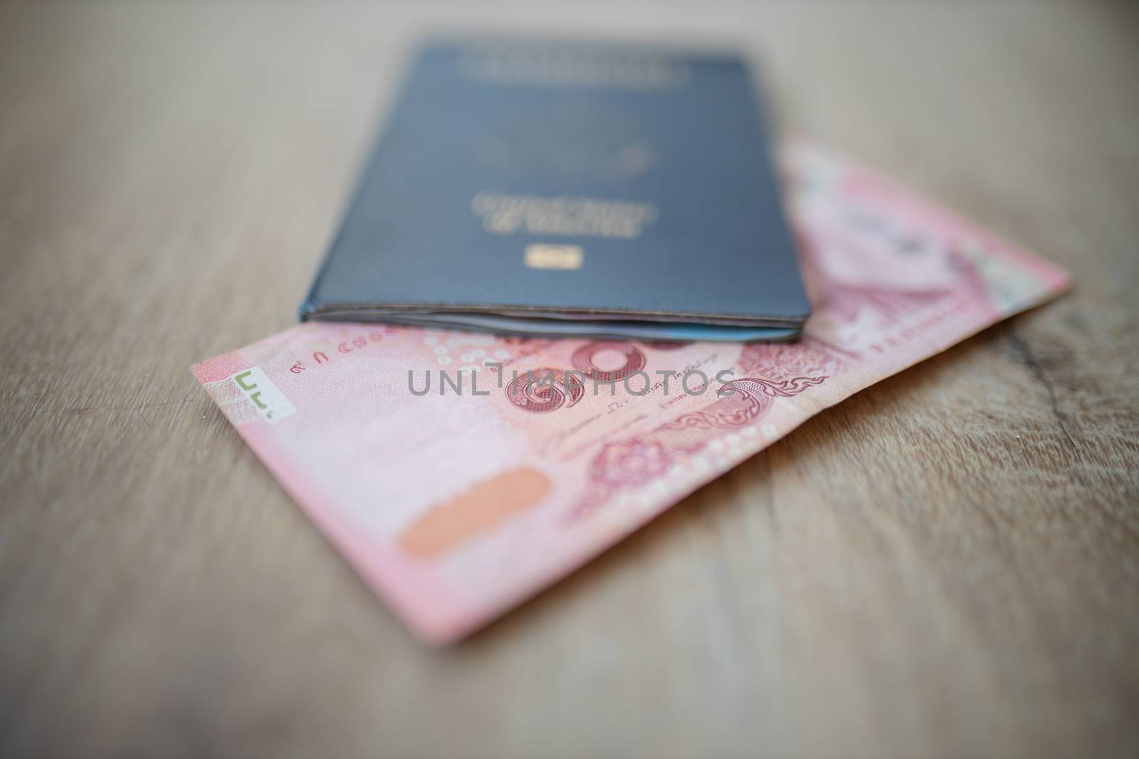 Picture of a 100 Thai Baht Bill -with the number 100 in Thai- Partially Inside a blurry United States of America Passport
