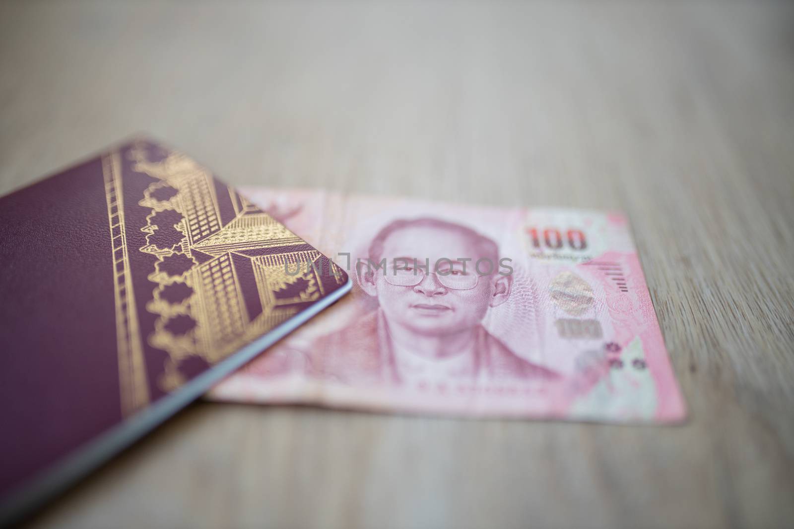 Picture of a 100 Thai Baht Bill Partially Inside a blurry Sweden Passport, showing the face of Bhumibol Adulyadej