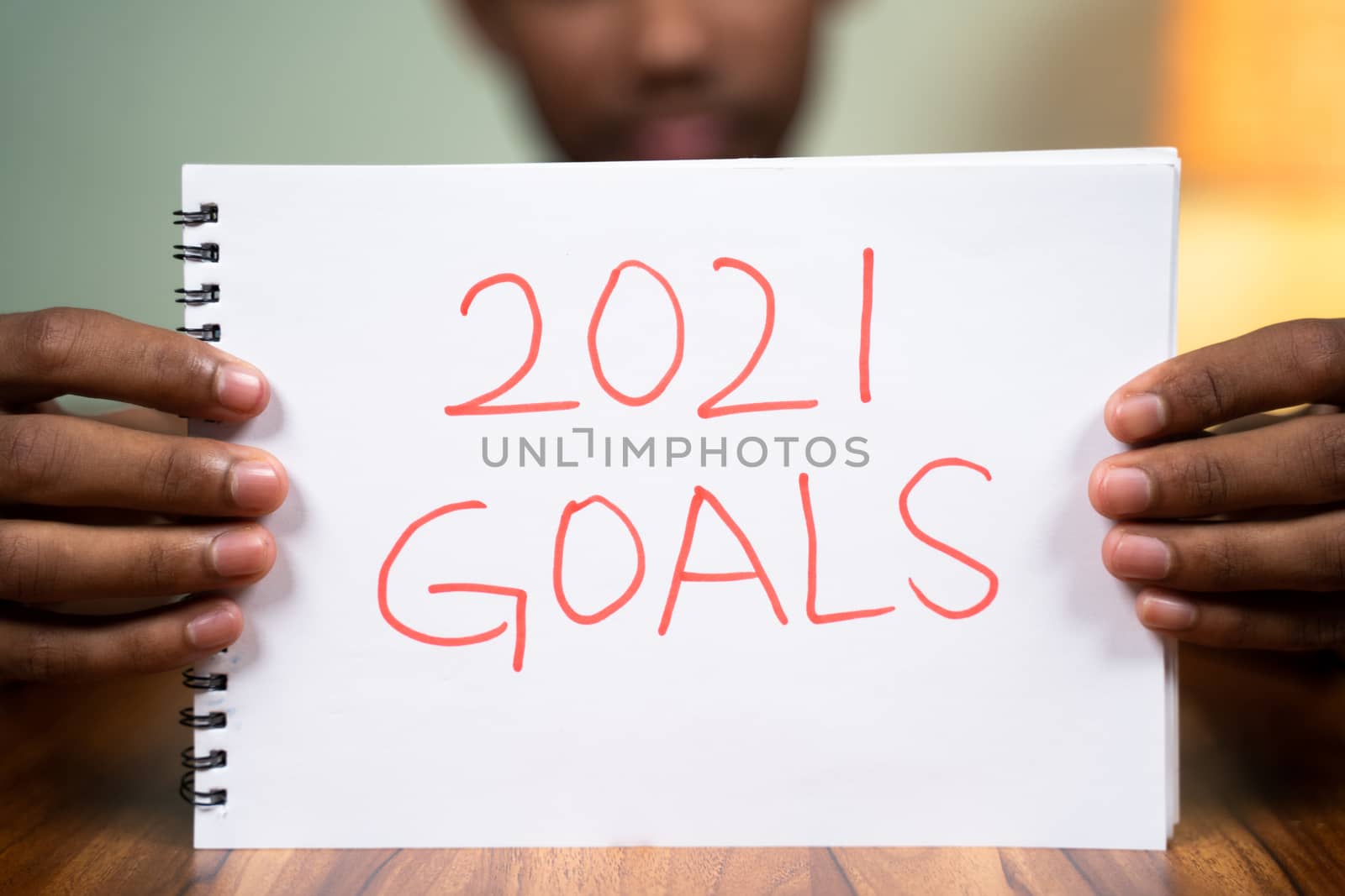 Man on table holding 2021 goals book in front of camera - concept of planning 2021 new year goals
