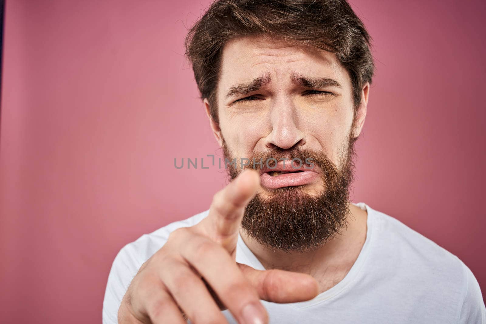 bearded man in white t-shirt emotions displeased facial expression studio pink background by SHOTPRIME