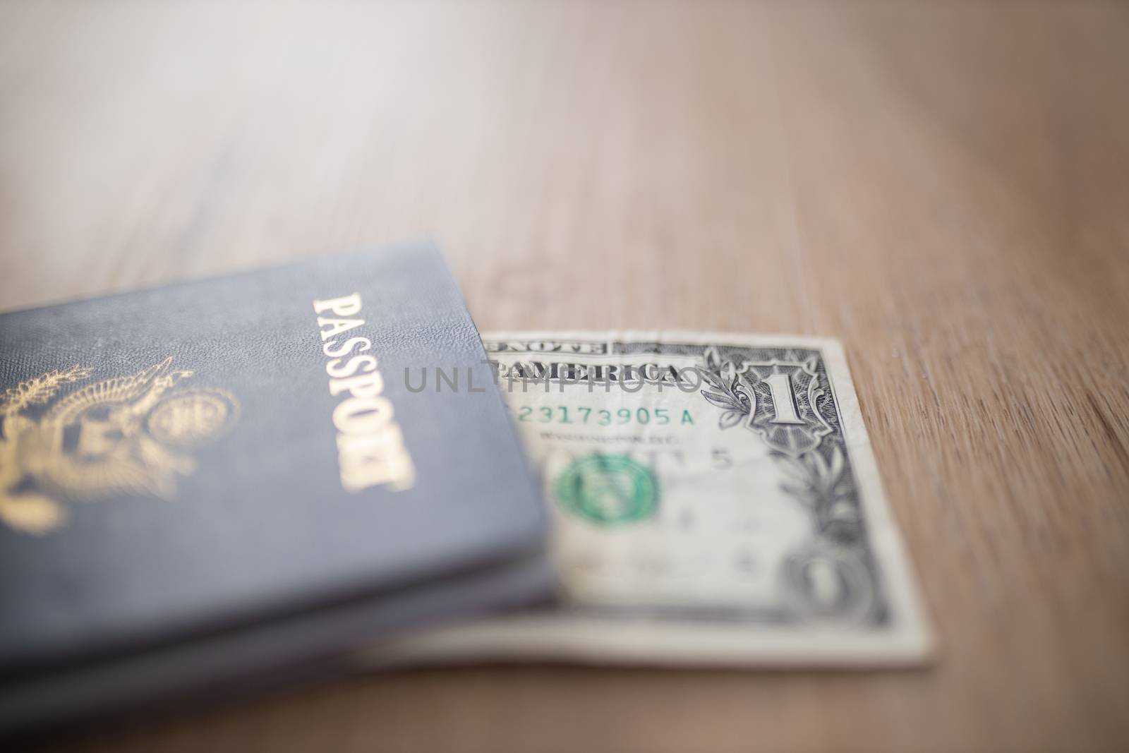 One-Dollar Bill Partially under a United States of America Passport on a Wooden Table