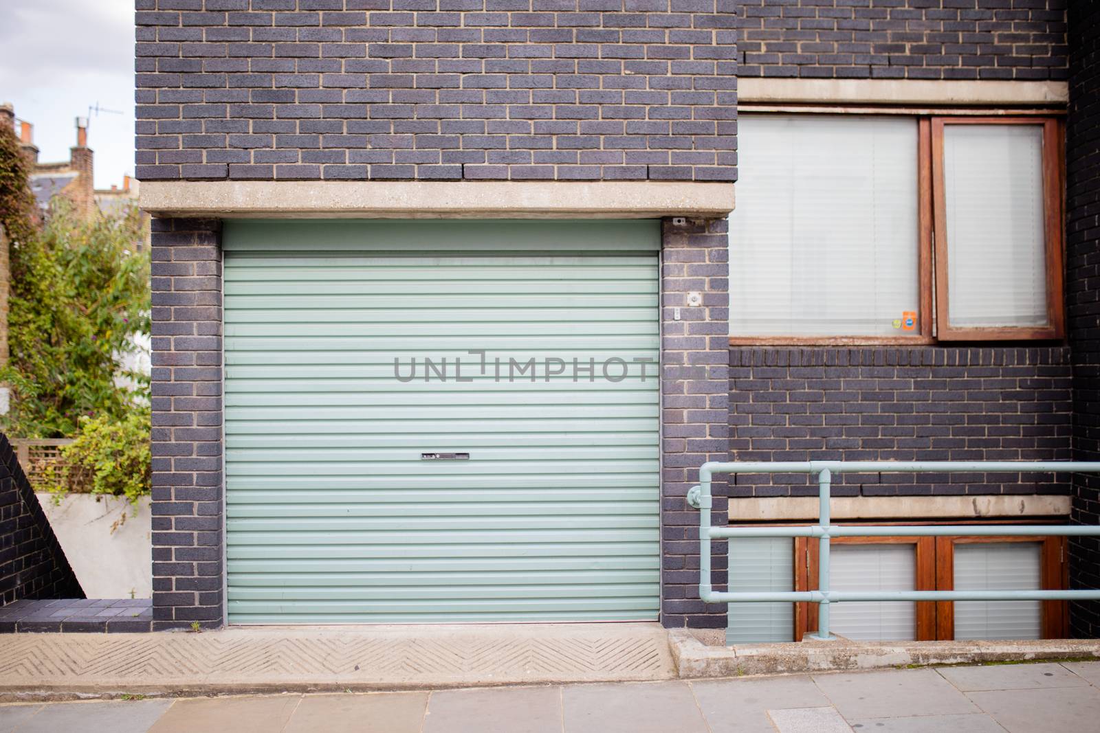 Landscape View of the Garage Door of a Dark Colour Brick Building with trees in the background and from London, UK