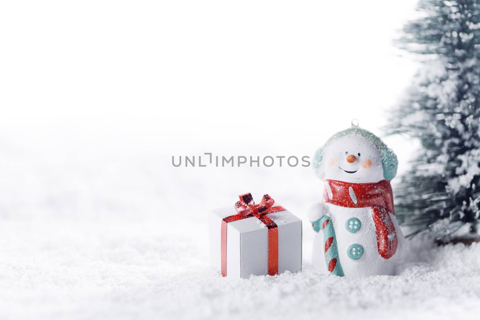 Small cute snowman with gift in fir forest under falling snow
