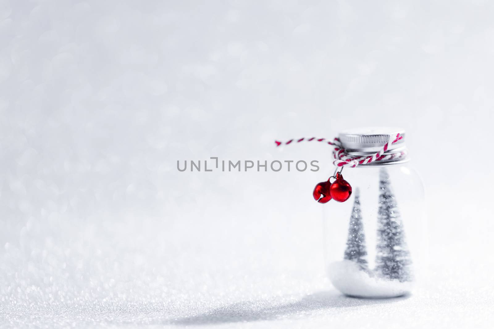 Christmas ornaments of glass jar with striped ribbon , bells and fir trees on snow inside on glitter background