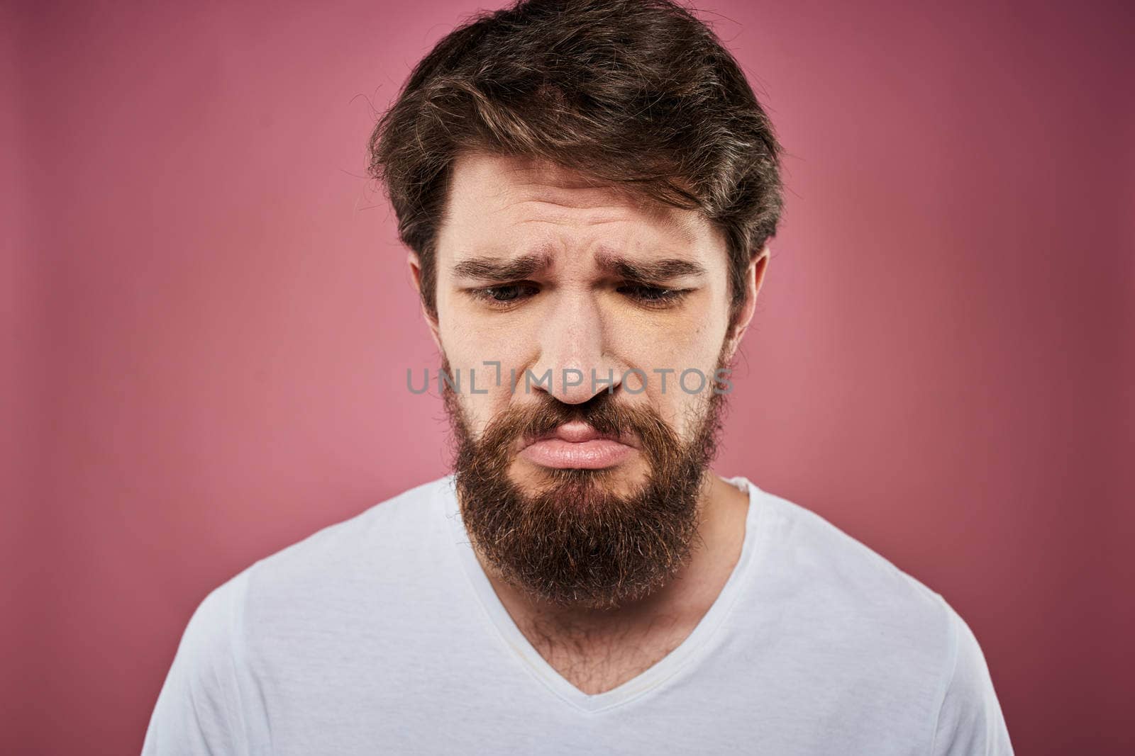 Emotional bearded man in white T-shirt discontent pink background. High quality photo