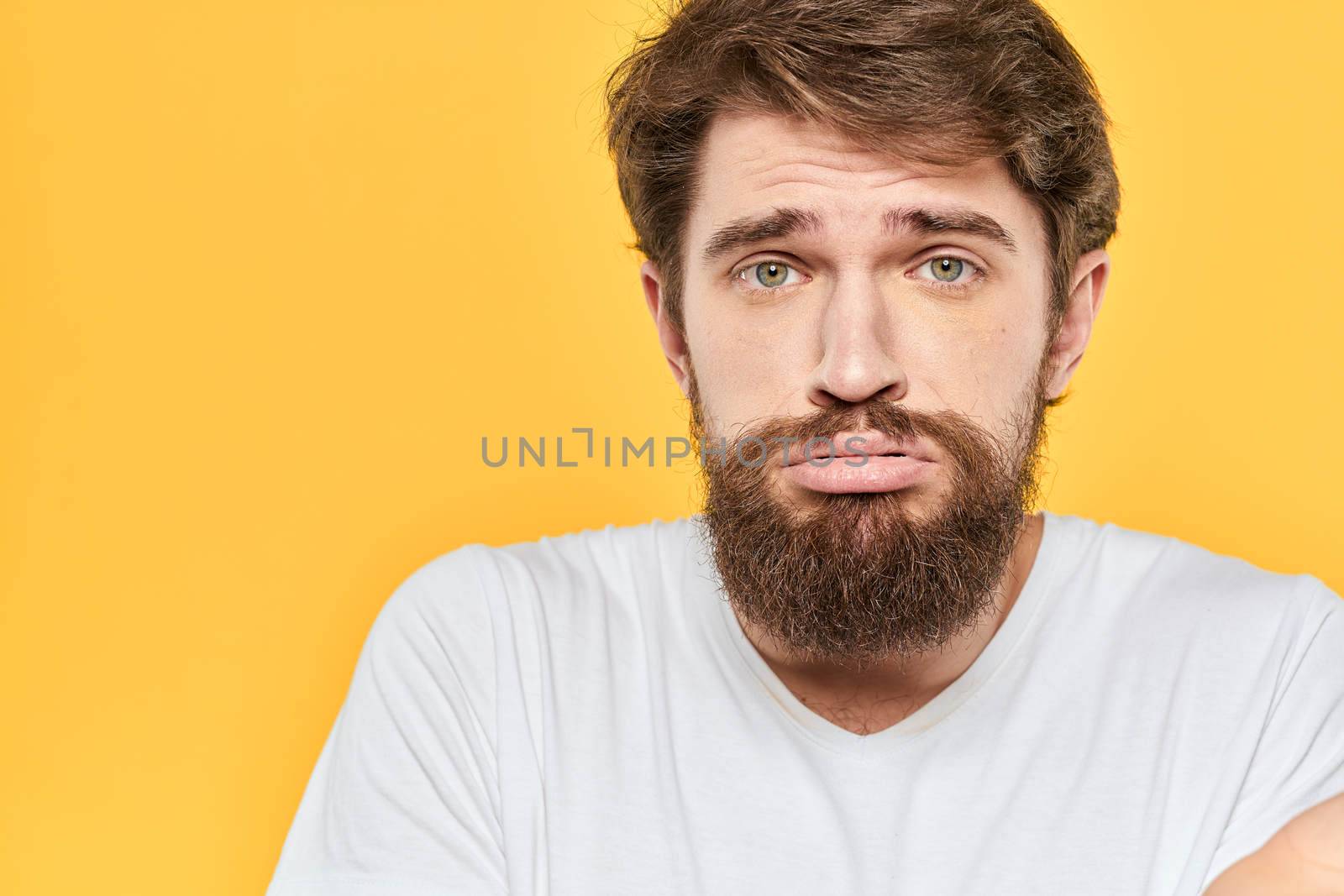 Man in white t-shirt emotions studio gestures with hands displeased facial expression yellow background. High quality photo