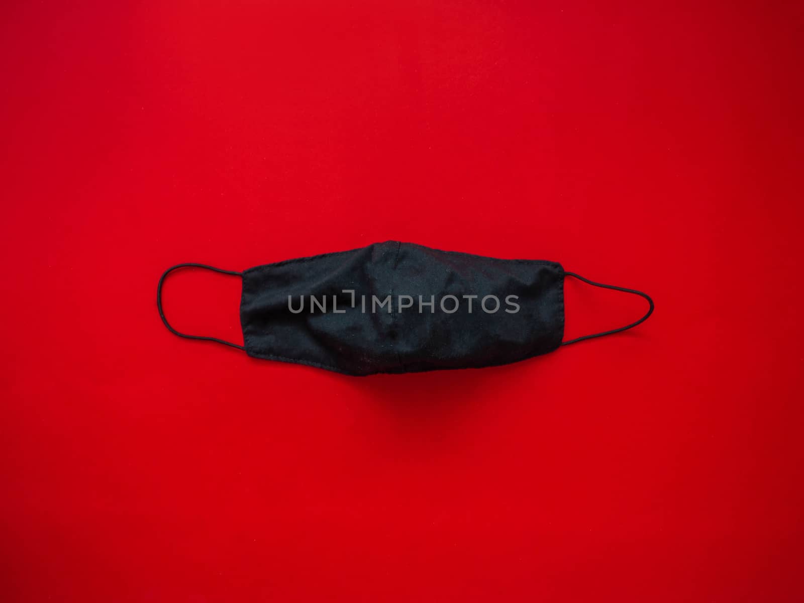 A black cloth mask for protection against saliva and dust droplets placed on a red background. During the virus spread heavily