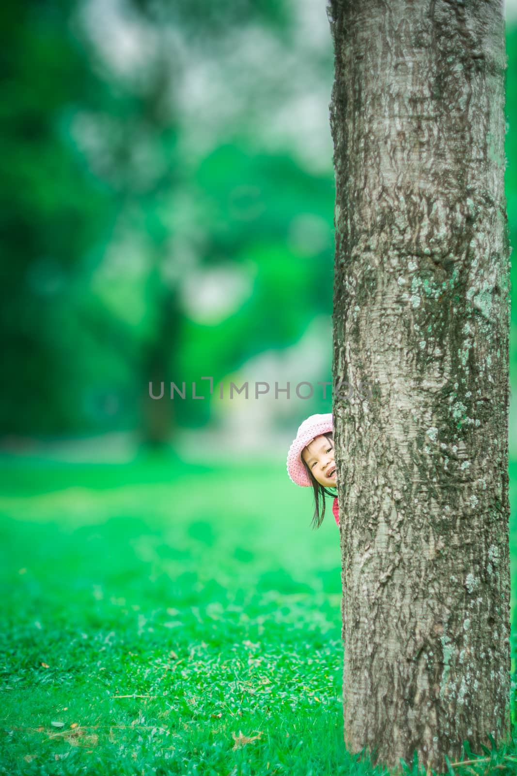 little girl sneaking behind the tree in the forest by domonite