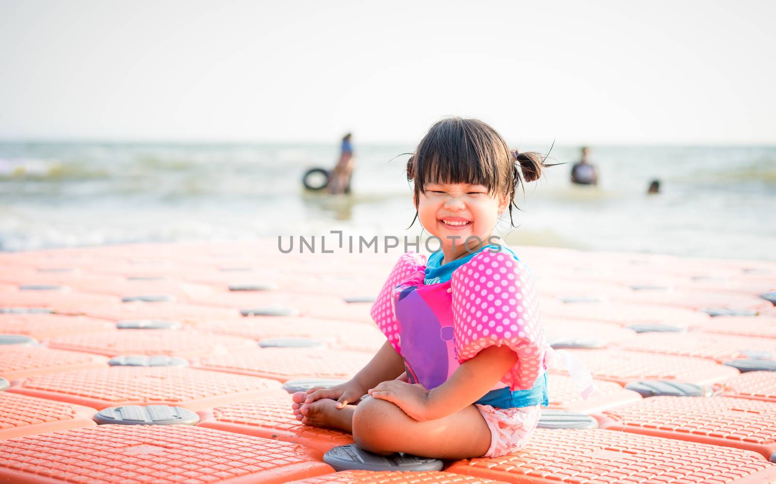 little asian girl wearing inflatable sleeves sitting on the beach