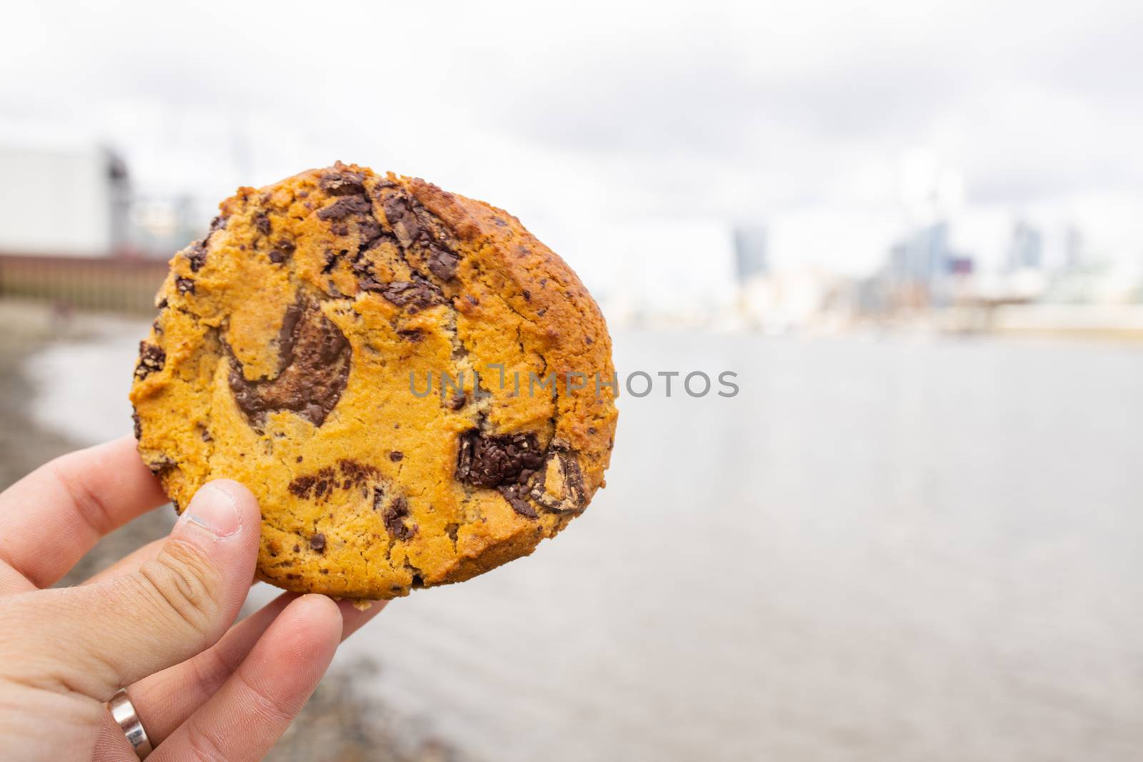 Landscape View of a Hand Holding a Chocolate Chips Cookie with a Blurry River Thames and CIty as Background