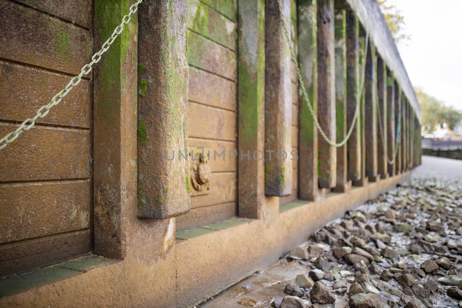 Landscape View of the ground covered in gray rocks, alongside an Orange Concrete Wall Partially Covered by Moss and with chains hanging from it